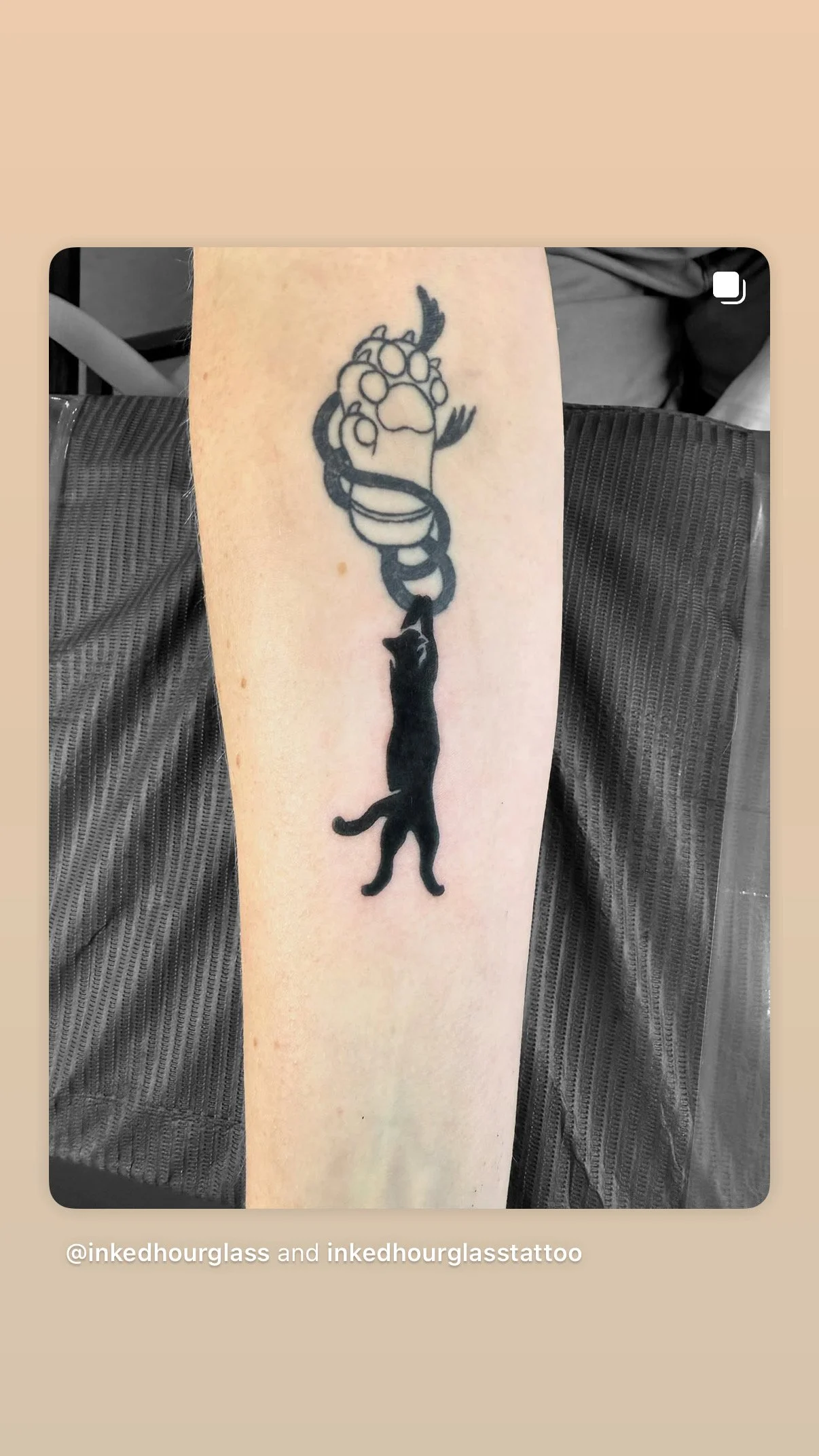 A tattoo of a black cat hanging from a paw print, with a snake intertwined around its body.