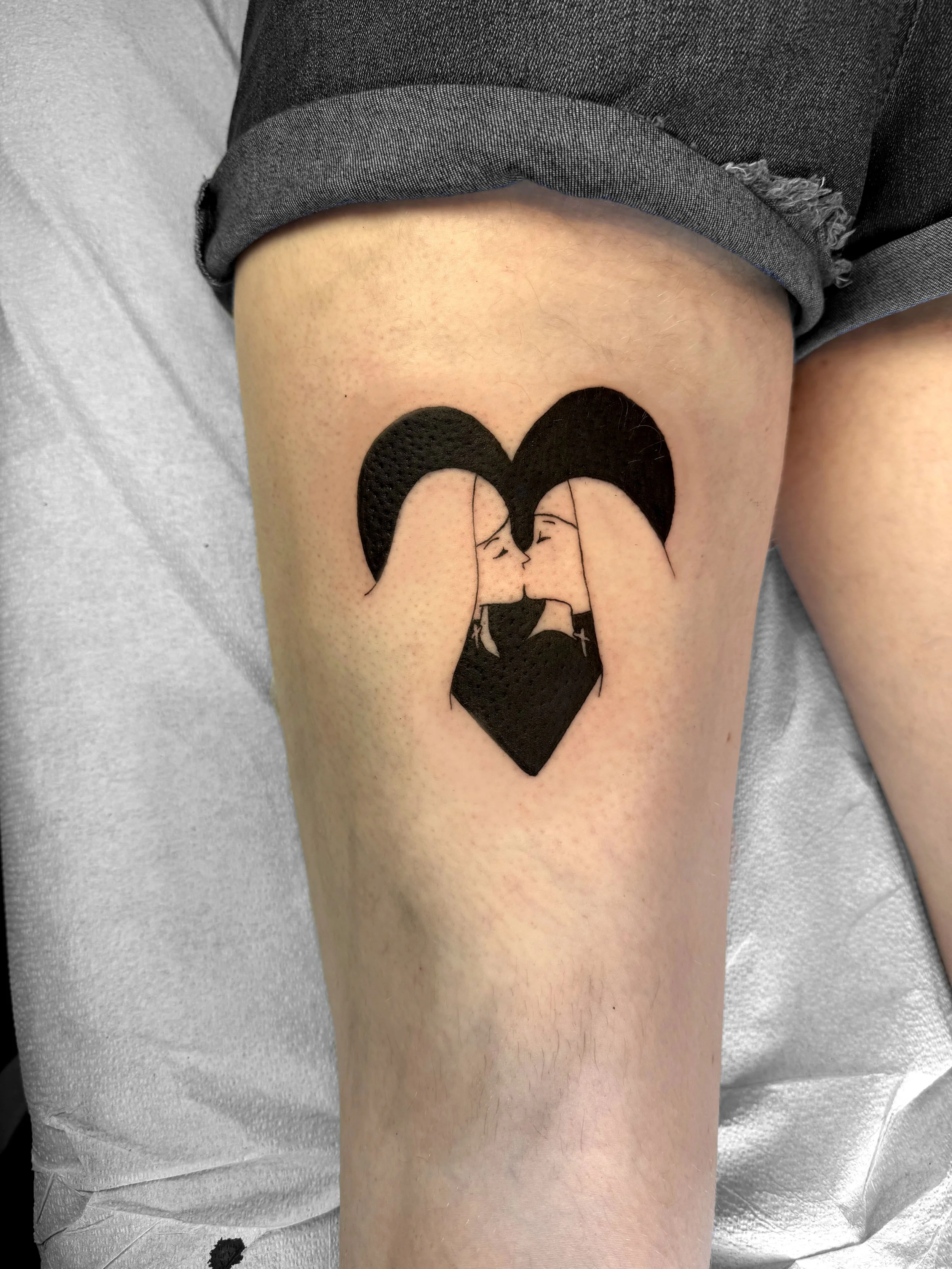 Tattoo of two women kissing, forming a shaped heart with their faces and hair.