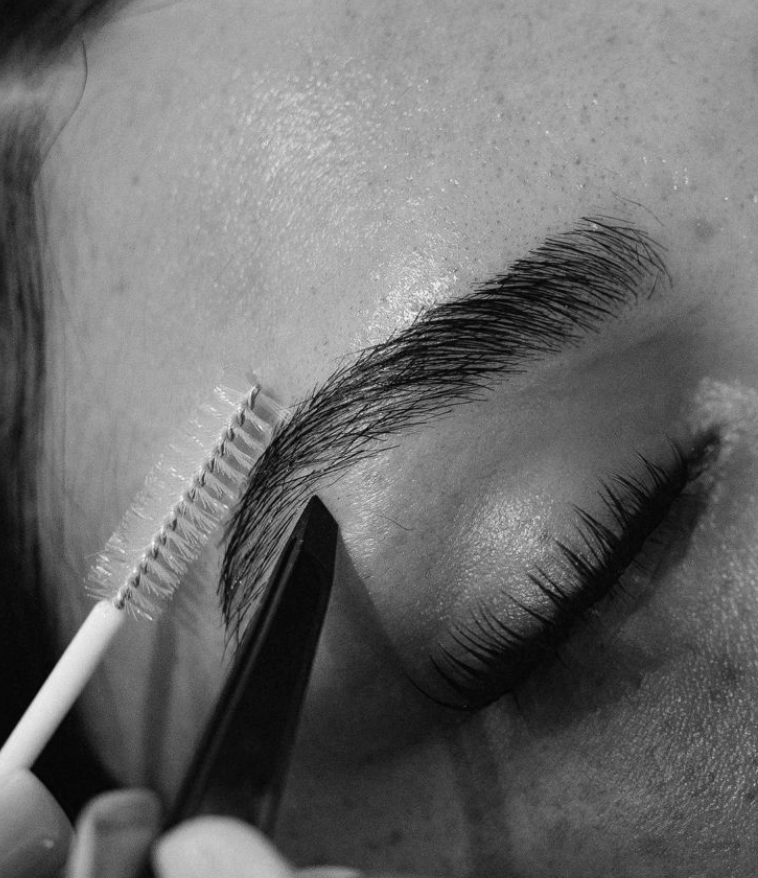 Close-up of a person applying eyelash extensions with a brush and tweezers.