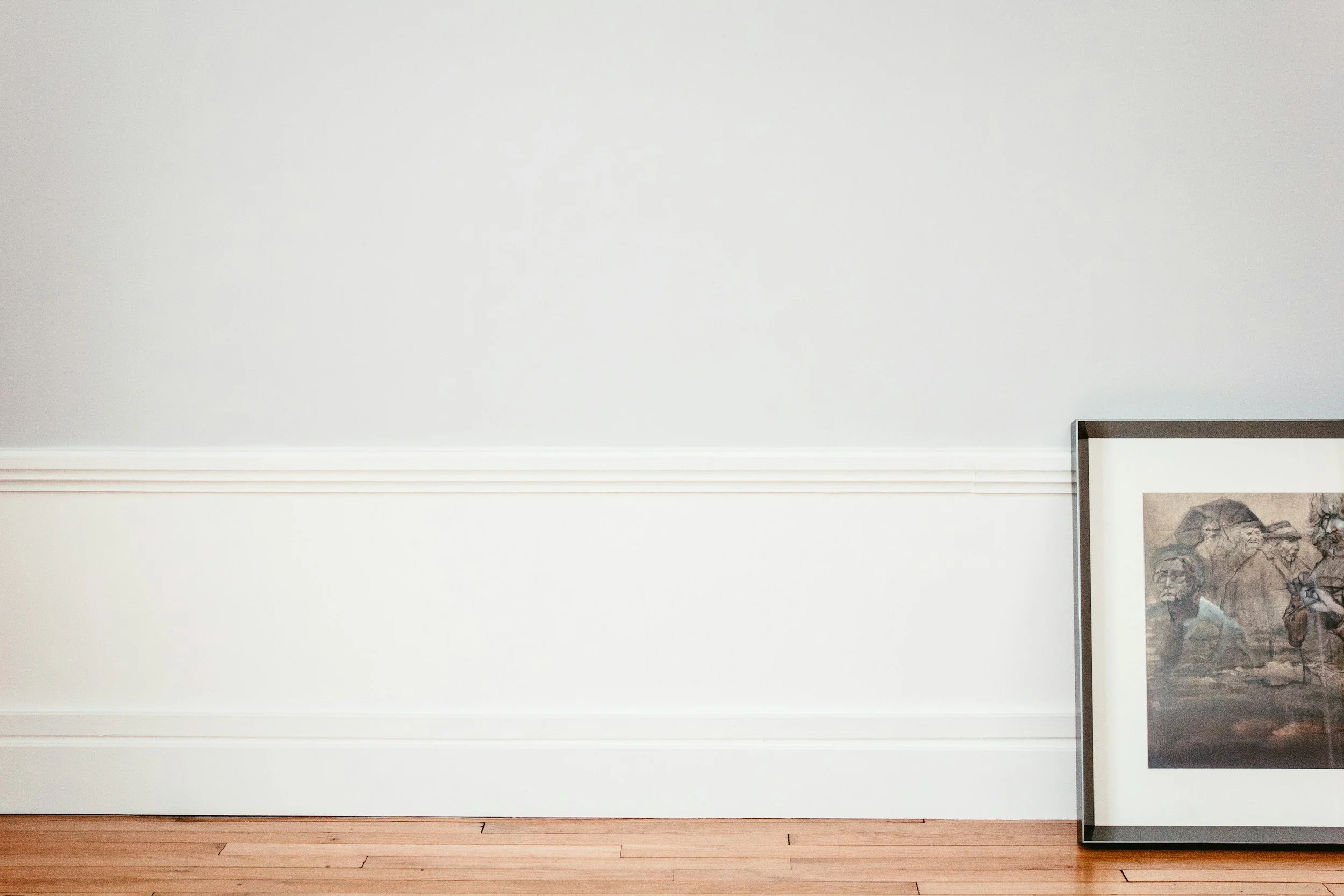 White wall with a framed artwork partially visible on the right side, wooden floor at the bottom.