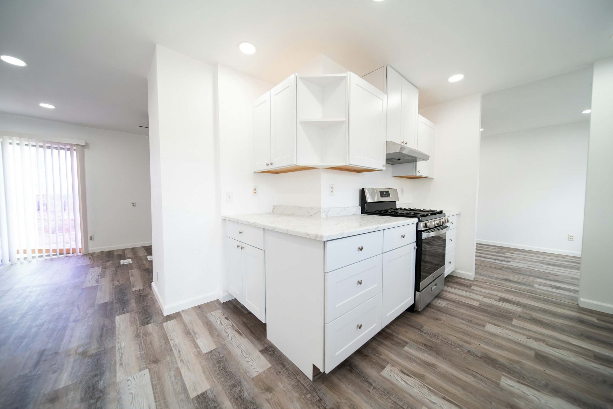 Modern kitchen with white cabinets, a marble countertop, stainless steel oven, and wood-style flooring.