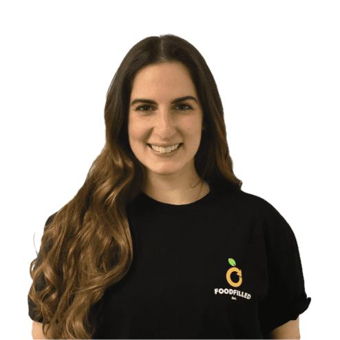 A woman with long brown hair smiling, wearing a black T-shirt with a logo that reads 'FOODFILLED' on the chest.