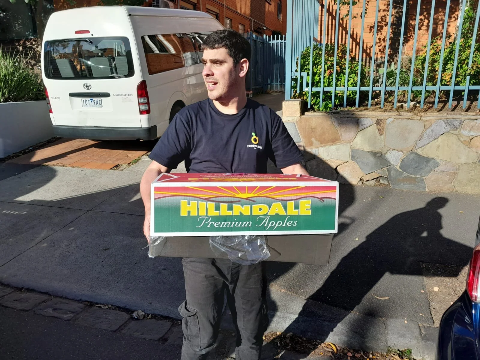 Man holding a box of Hilldale Premium Apples on sidewalk outside.