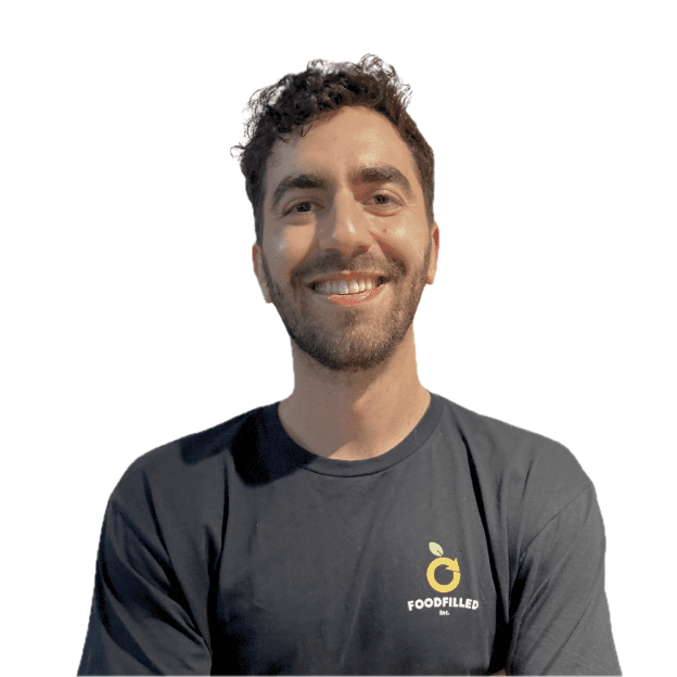 Smiling man with dark hair and beard wearing a dark gray t-shirt with a small yellow logo and the words 'FOODFILLED Inc.'