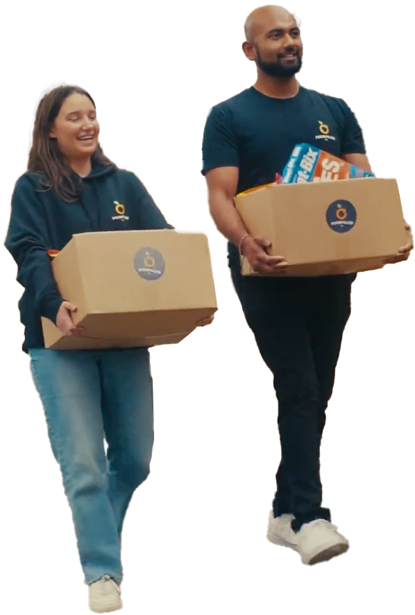 Two people smiling and holding large cardboard boxes with a logo, likely participating in a charity or donation event.