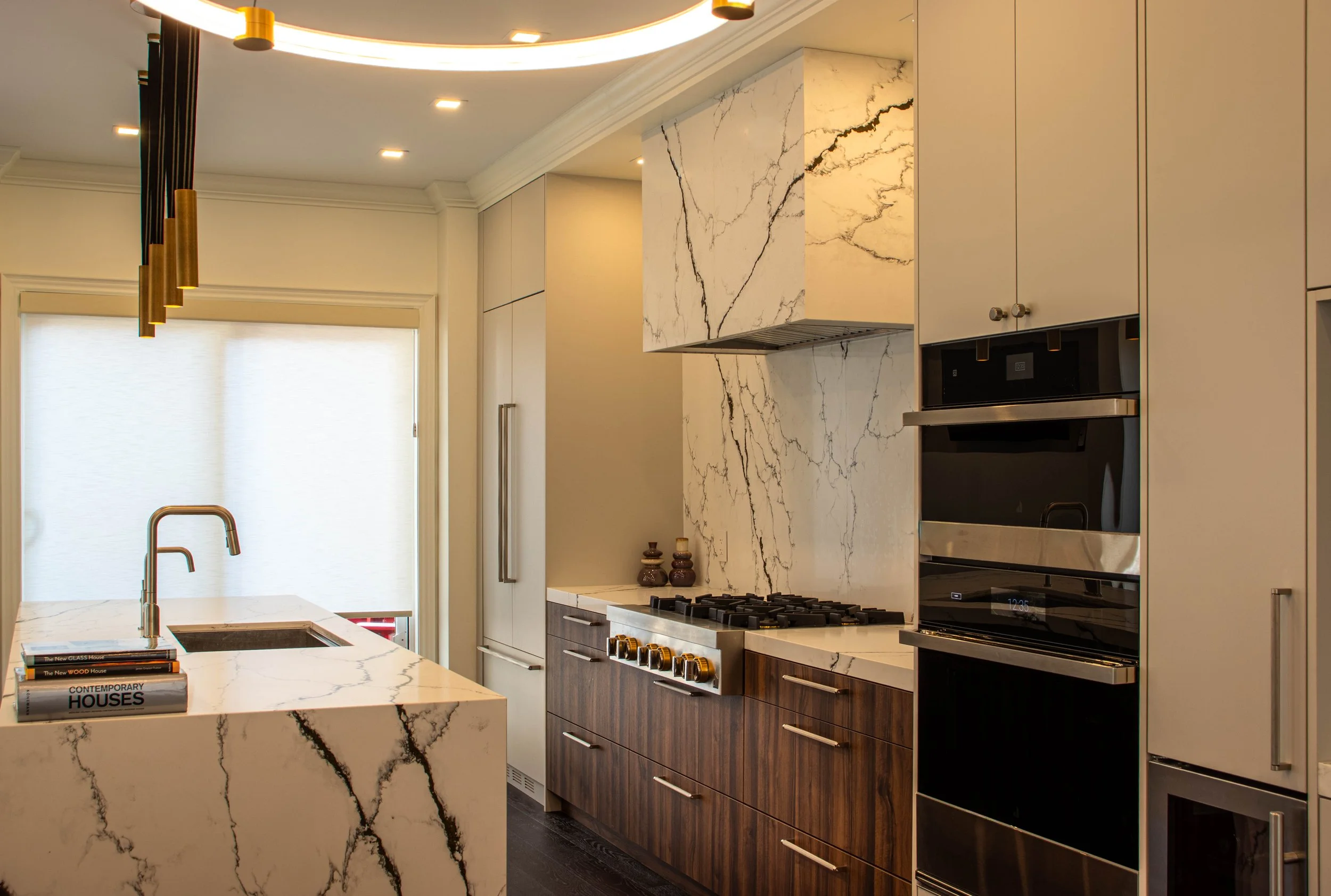 Luxury modern kitchen interior design in Toronto featuring marble waterfall island, custom wood cabinetry, and integrated appliances