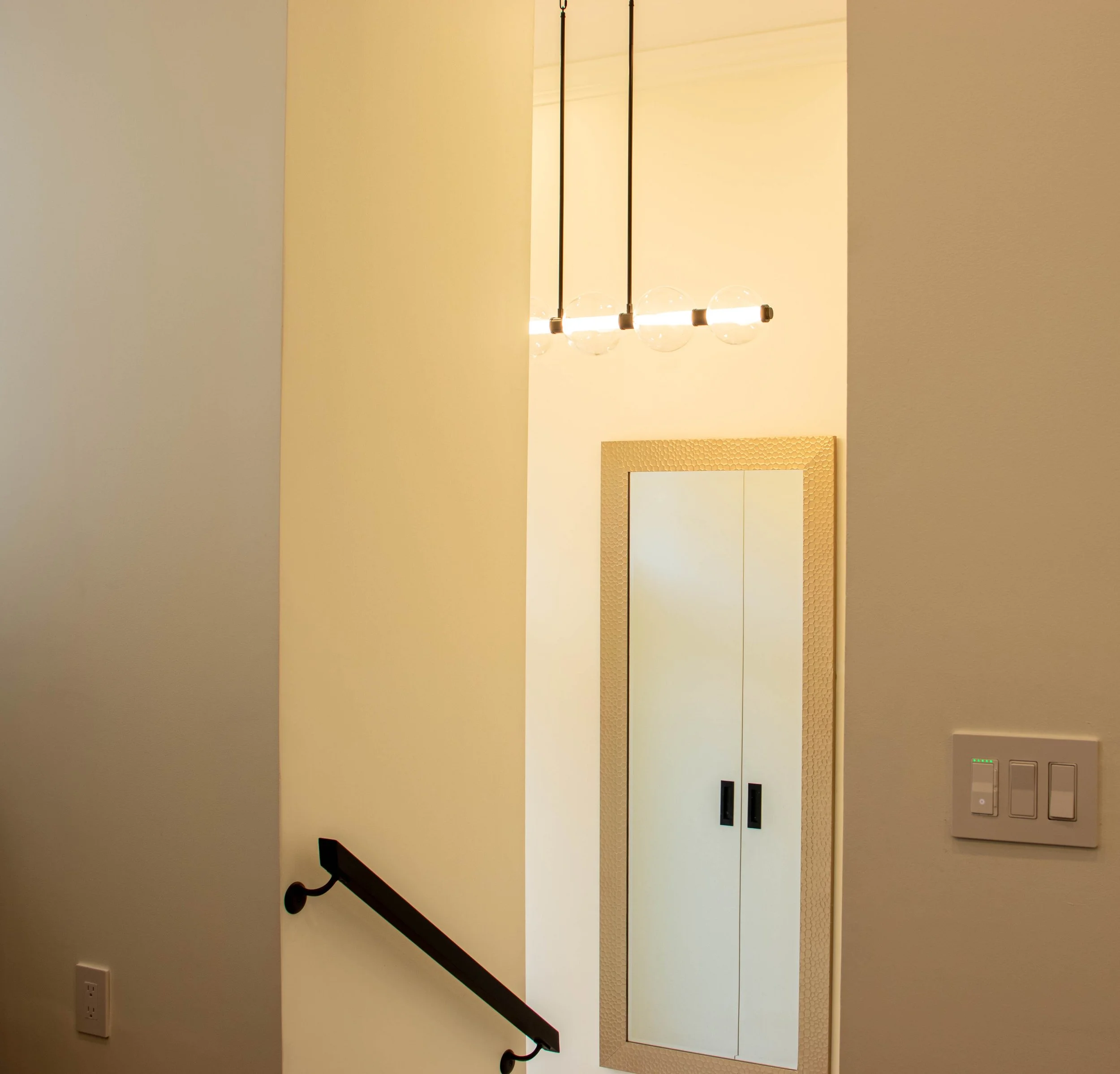 Modern stair landing showcasing custom built-in storage with integrated handles, warm neutral walls, minimalist pendant lighting, and clean architectural detailing in a contemporary home.