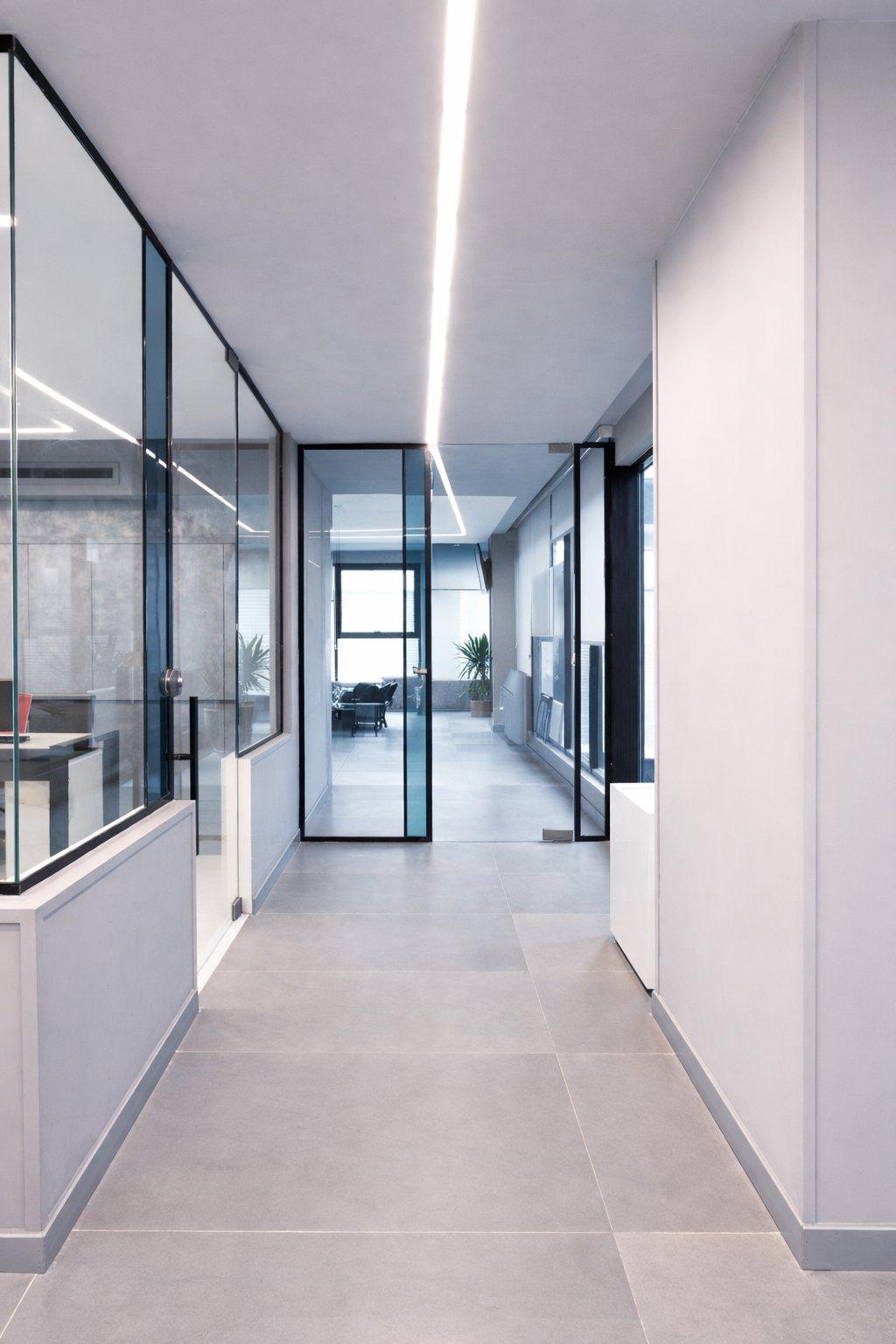 Minimal office corridor with glass partitions, linear LED ceiling lighting, and a clean, modern commercial interior design.