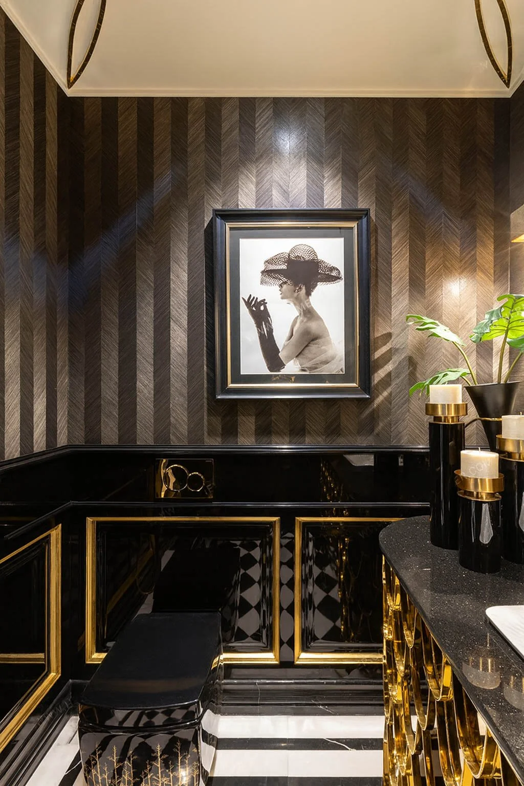 Luxury art deco powder room showcasing black lacquer cabinetry, gold detailing, herringbone wall treatment, graphic tile flooring, and curated artwork in an elegant high-end residential interior.