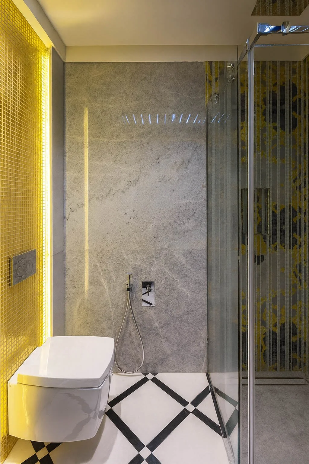 Modern luxury powder room featuring a wall-hung toilet, glass-enclosed shower, marble wall surfaces, geometric tile flooring, and integrated ambient lighting for a refined contemporary interior.