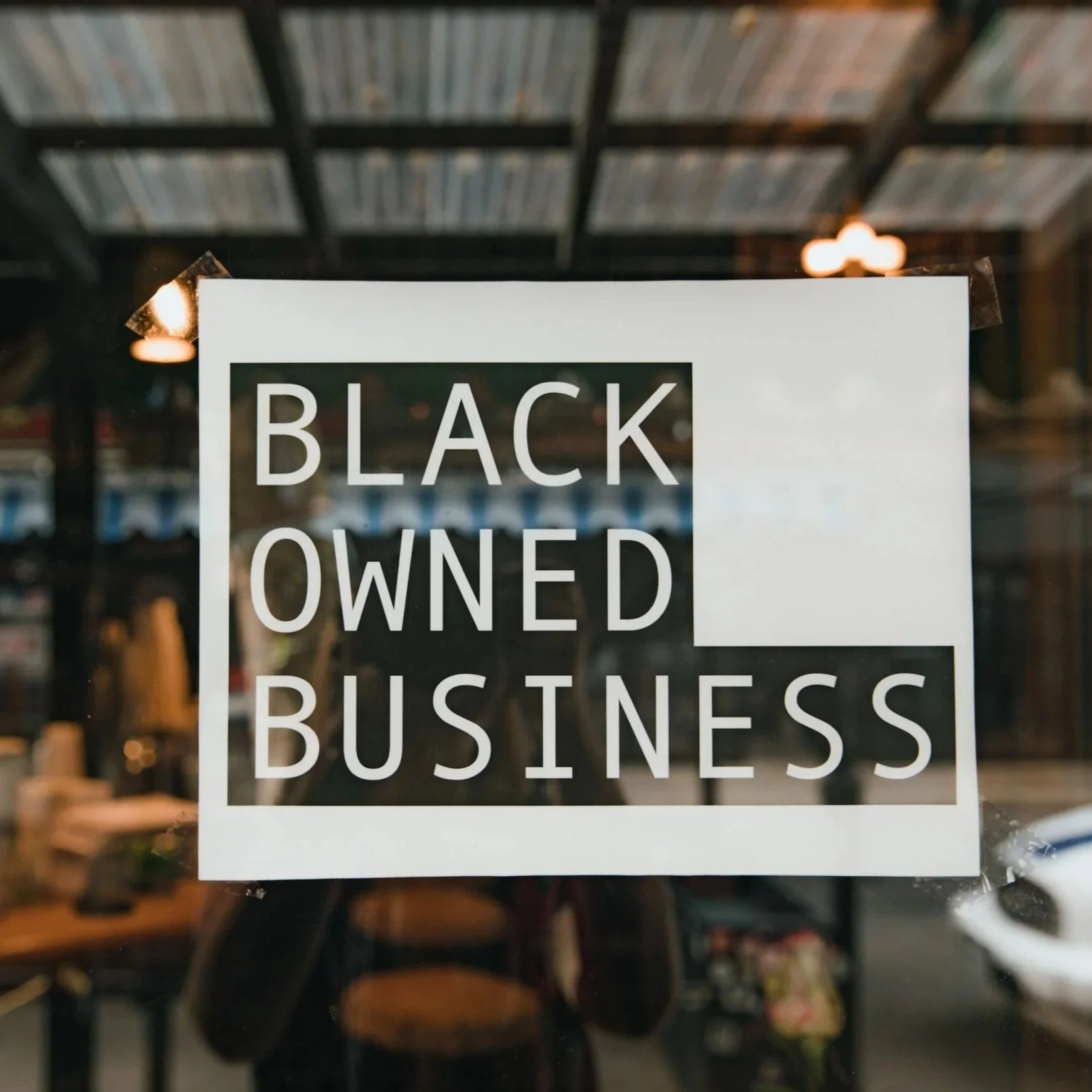 A sign on a glass door or window reading 'Black Owned Business' with the interior of a store visible behind the glass.