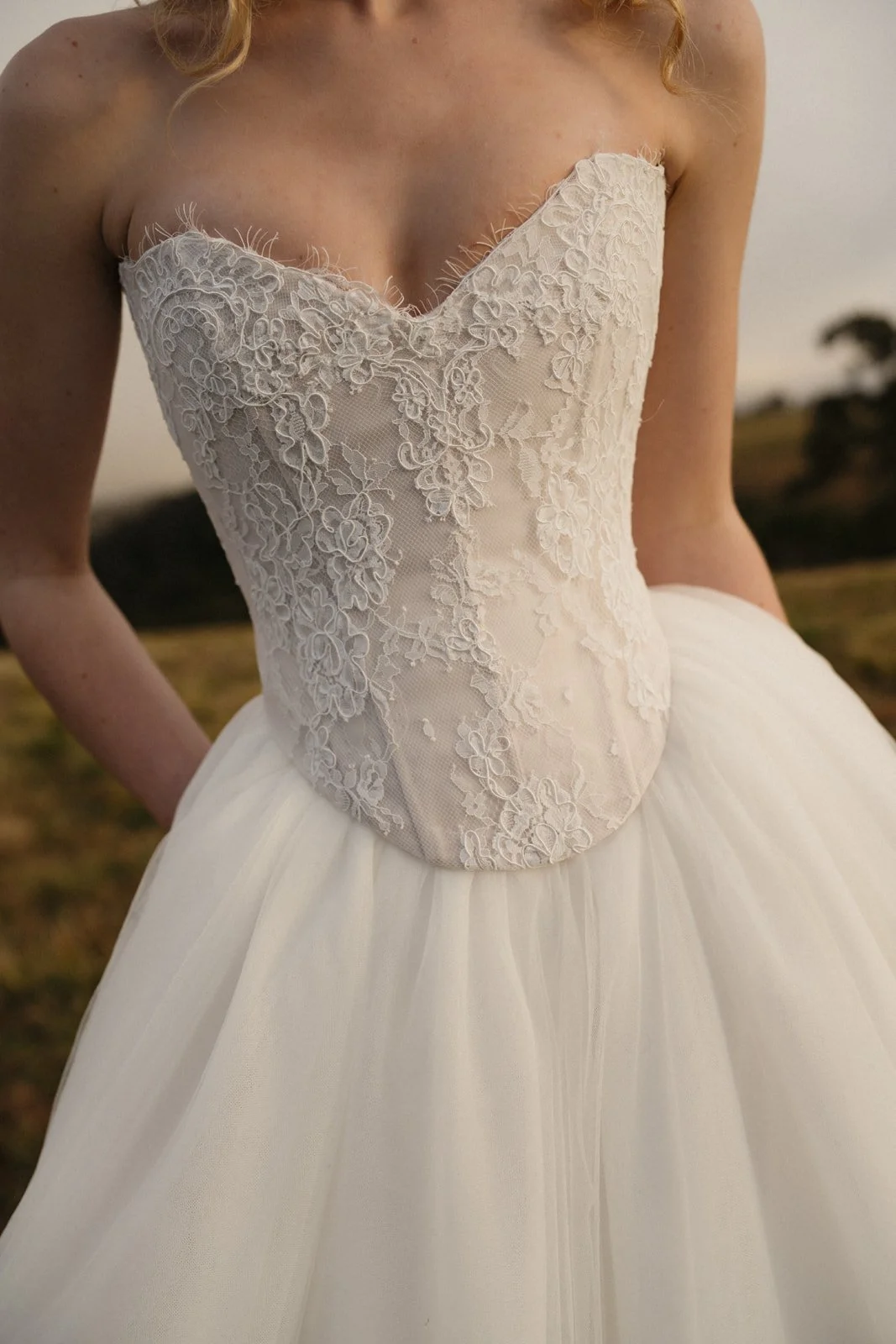Close-up of a wedding dress with a lace, strapless bodice and a full, tulle skirt, outdoors during sunset.
