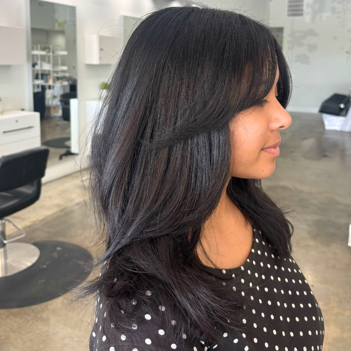 Side profile of a woman with long, dark, shiny hair in a salon setting.