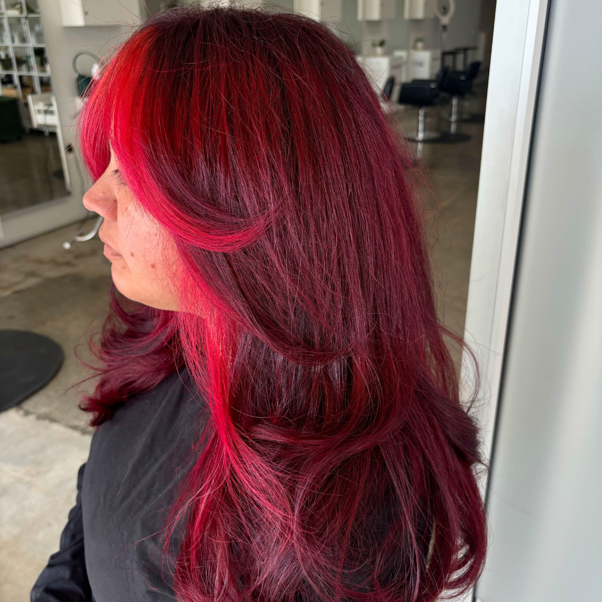 Woman with long, wavy hair dyed in shades of dark red, pink, and purple, sitting in a salon.