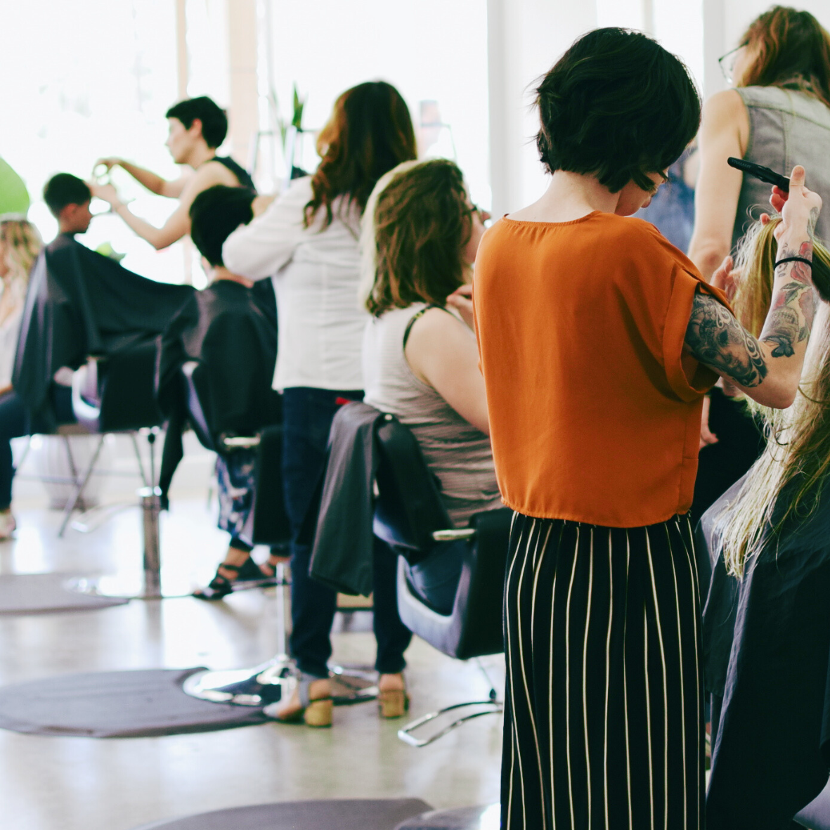 Women getting their hair styled at a salon, with clients seated and hairstylists working.