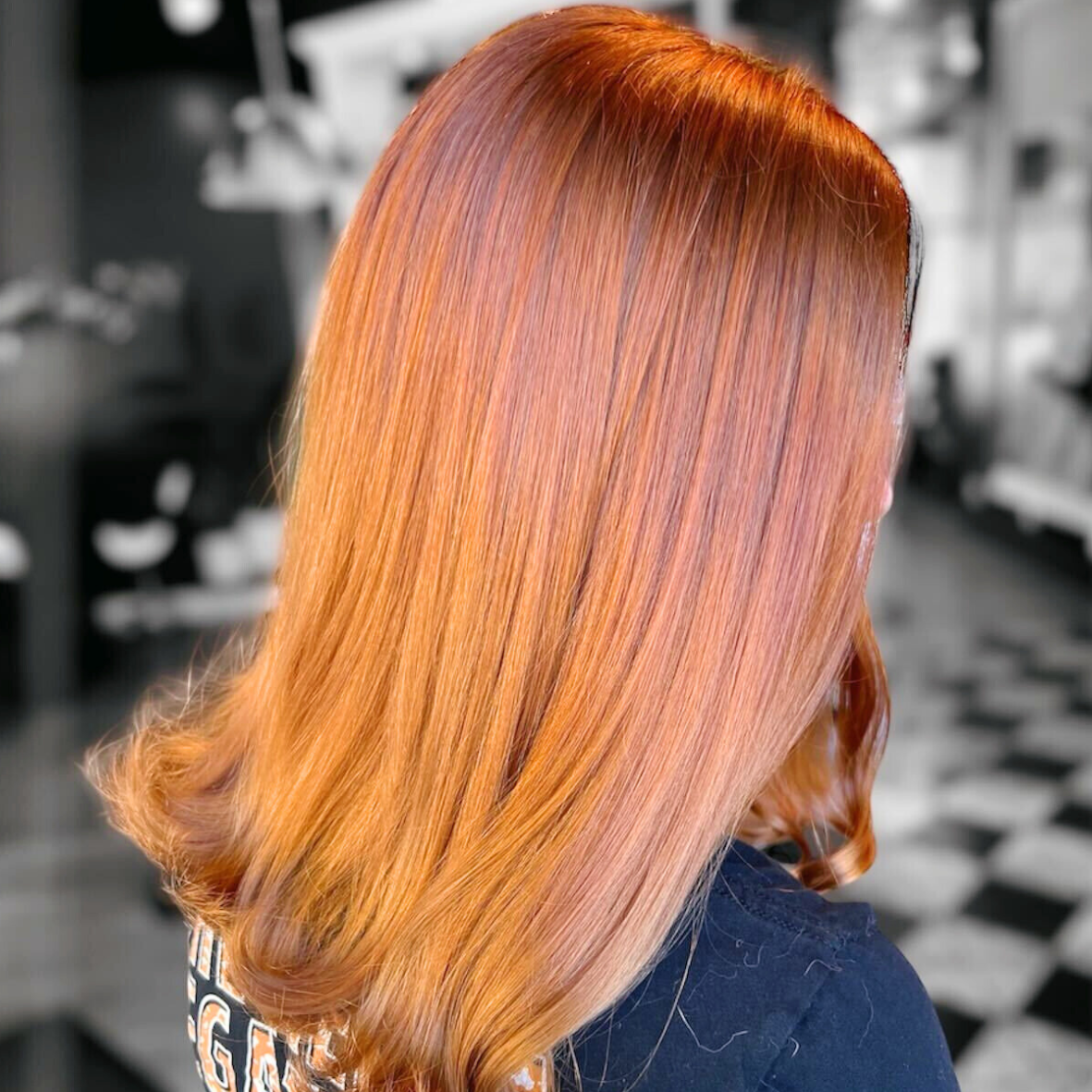 Side view of a woman with shiny, straight, orange hair styled straight with soft waves at the ends, in a salon setting.