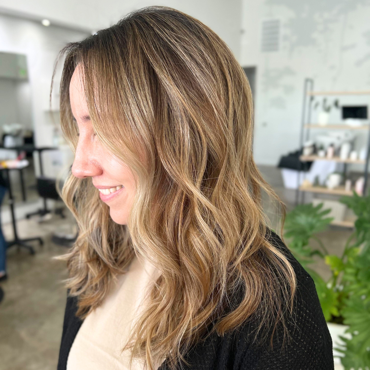Side profile of a smiling woman with wavy, ombré blonde hair in a salon setting.
