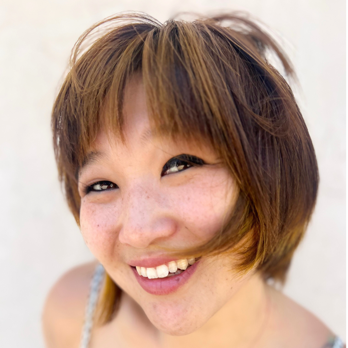 Close-up of a smiling woman with short, brown hair and freckles, looking at the camera.