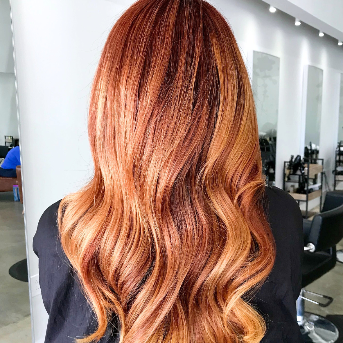Back view of a person with long, wavy, red hair in a salon setting.