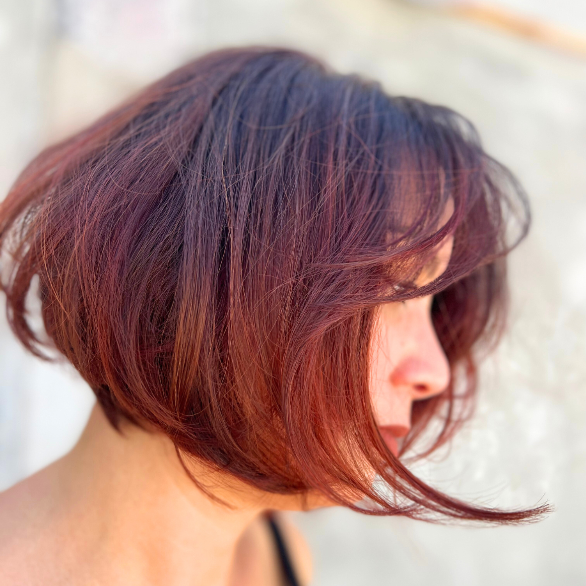 Side profile of a woman with shoulder-length, wavy hair with dark purple and reddish hues.