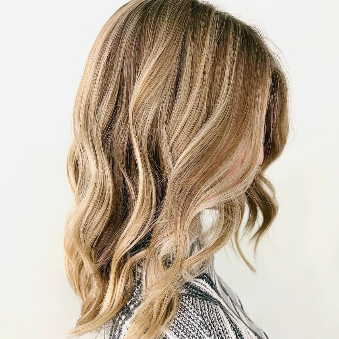 Side view of a woman with shoulder-length, wavy blonde hair. She is wearing a black and white patterned top.