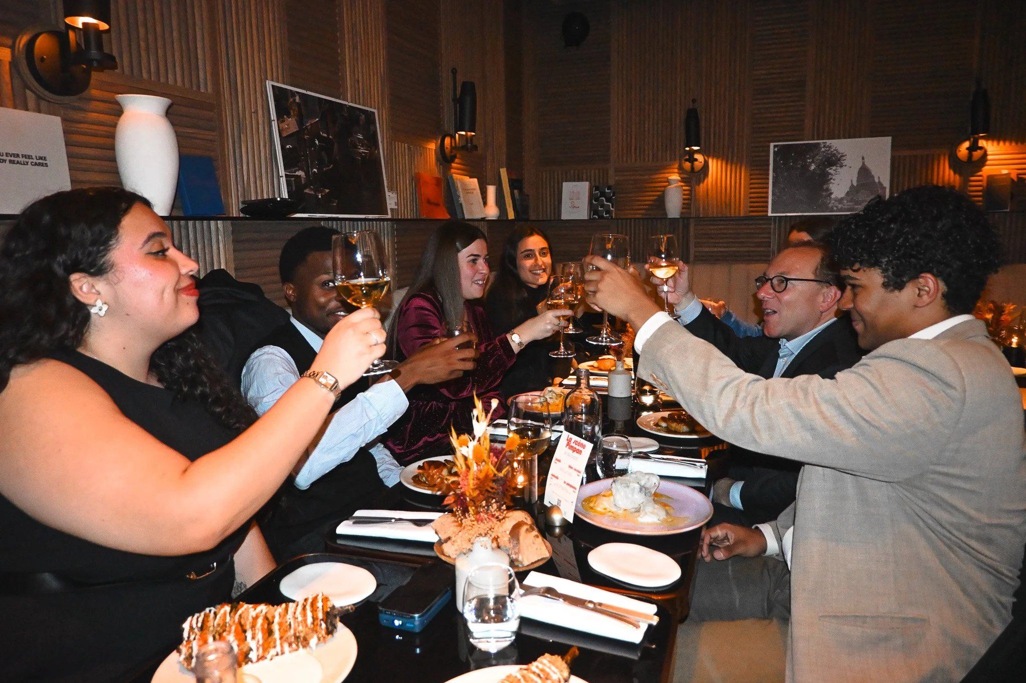Groupe de personnes à une table de dîner, levant leurs verres pour faire un toast, dans un restaurant ou un lounge élégant.