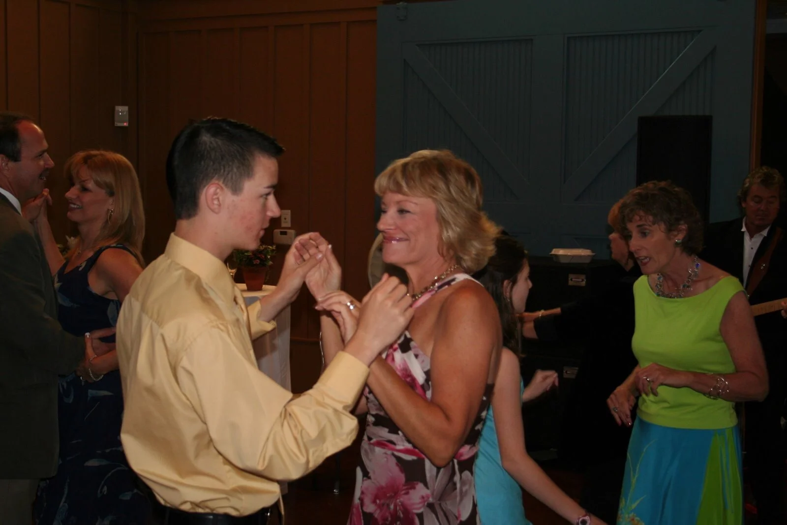 Young man and woman dancing together at an indoor party, with other couples dancing and socializing in the background.
