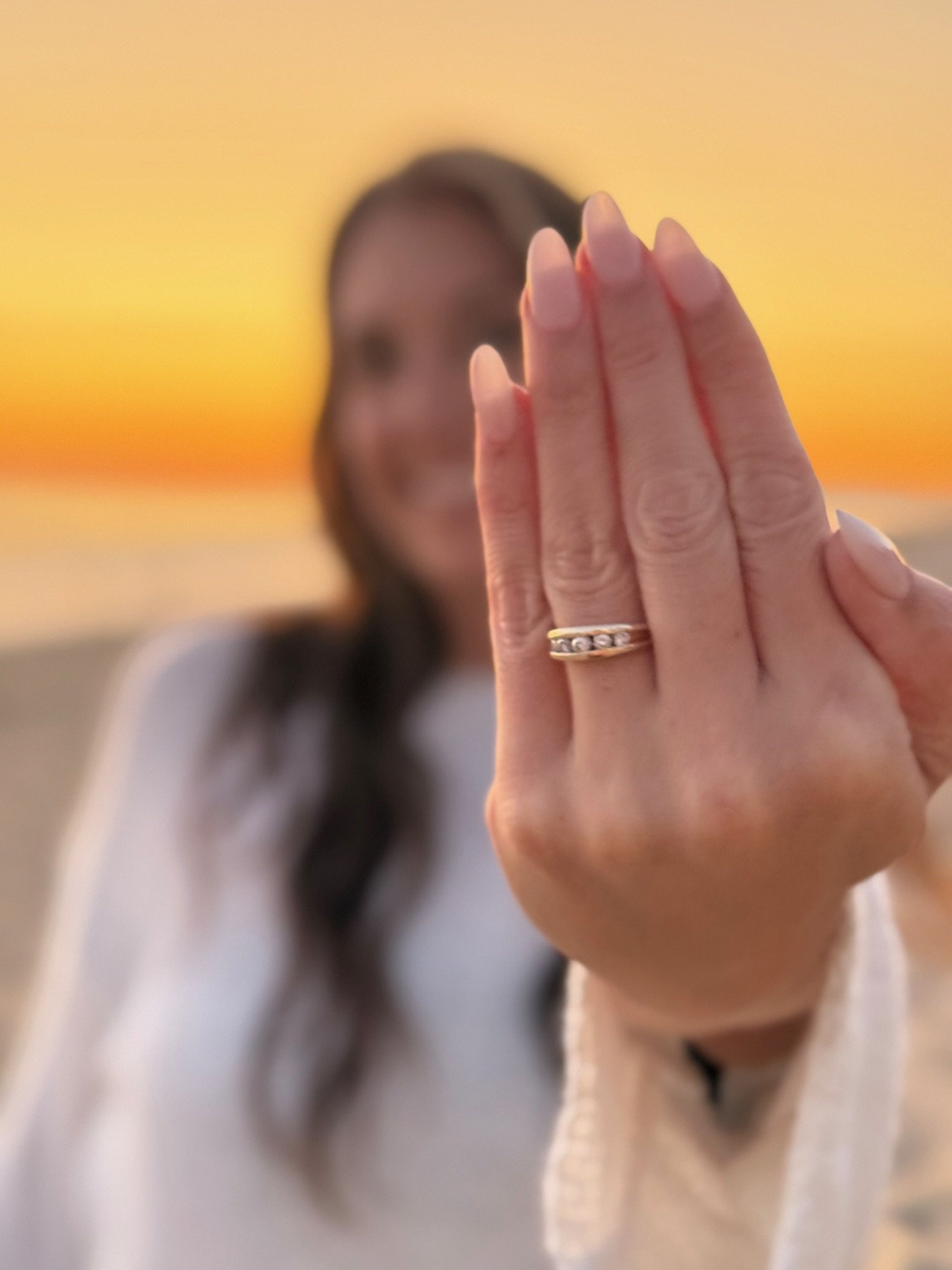 A woman showing her hand with a ring, outdoors during sunset.