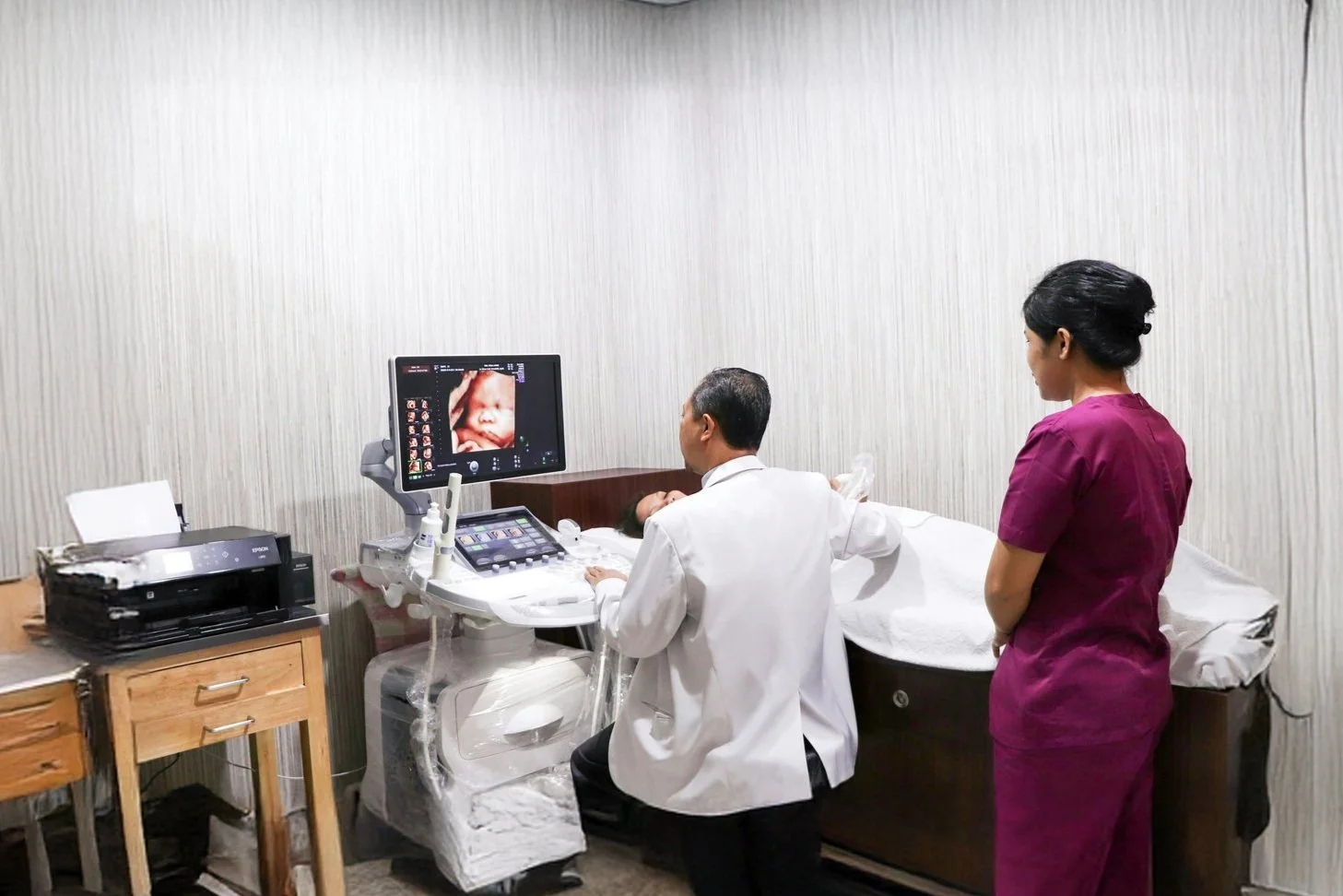 Medical professionals performing an ultrasound on a pregnant woman in a clinical room.