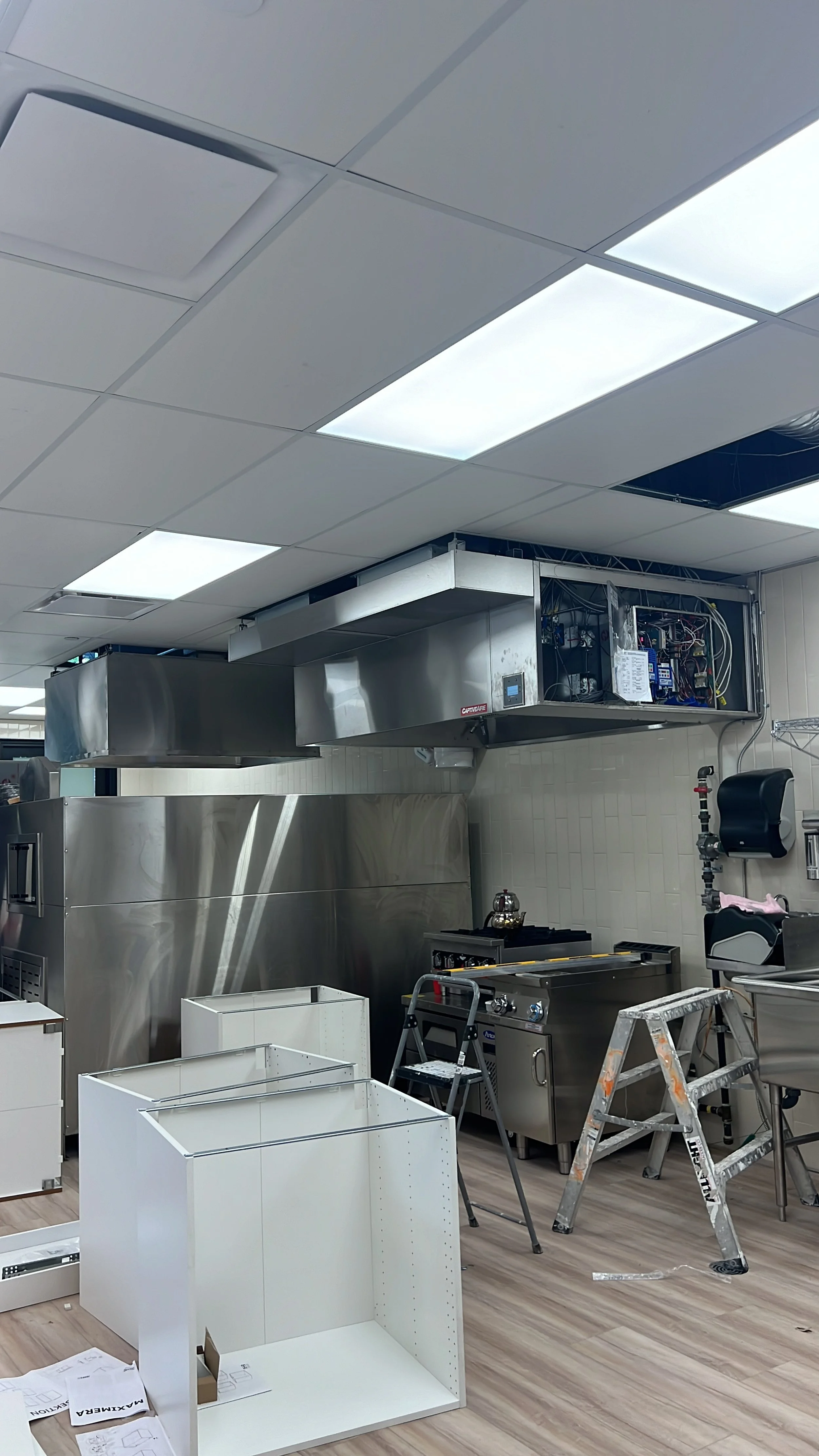 Kitchen under construction with stainless steel appliances, white cabinets, a ladder, and building materials.