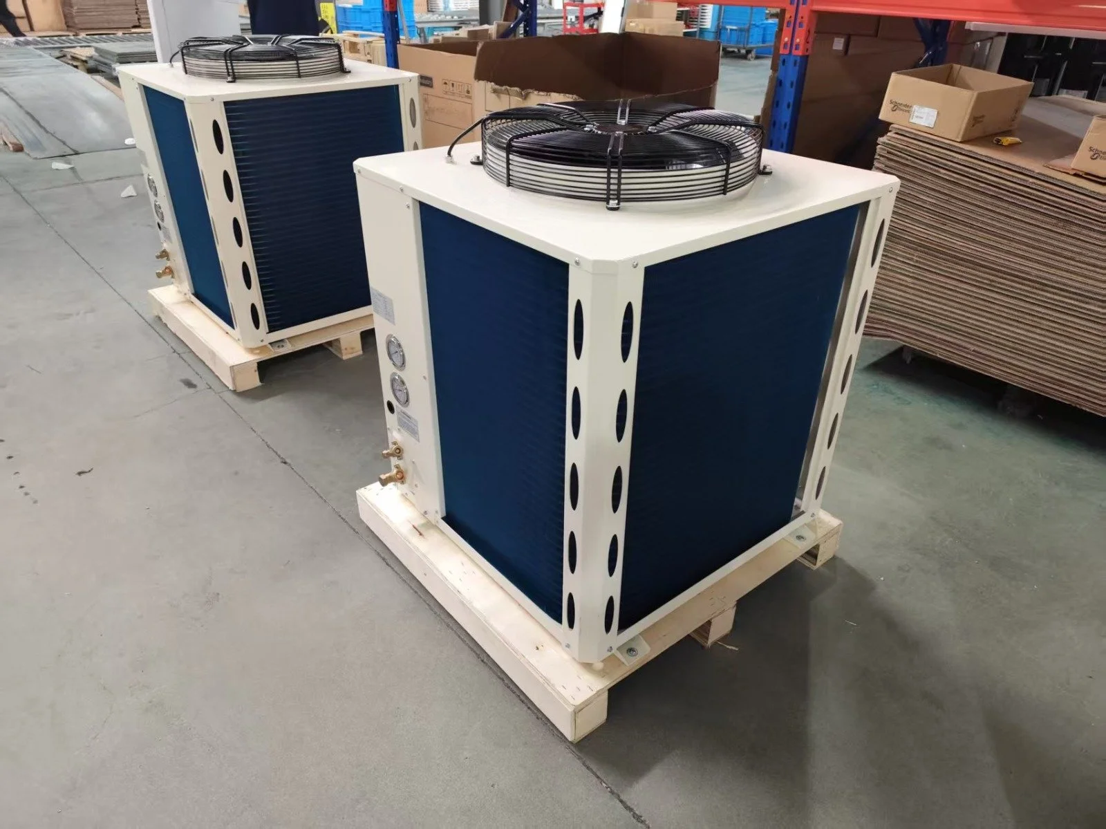 Two industrial air conditioning units on wooden pallets in a warehouse.