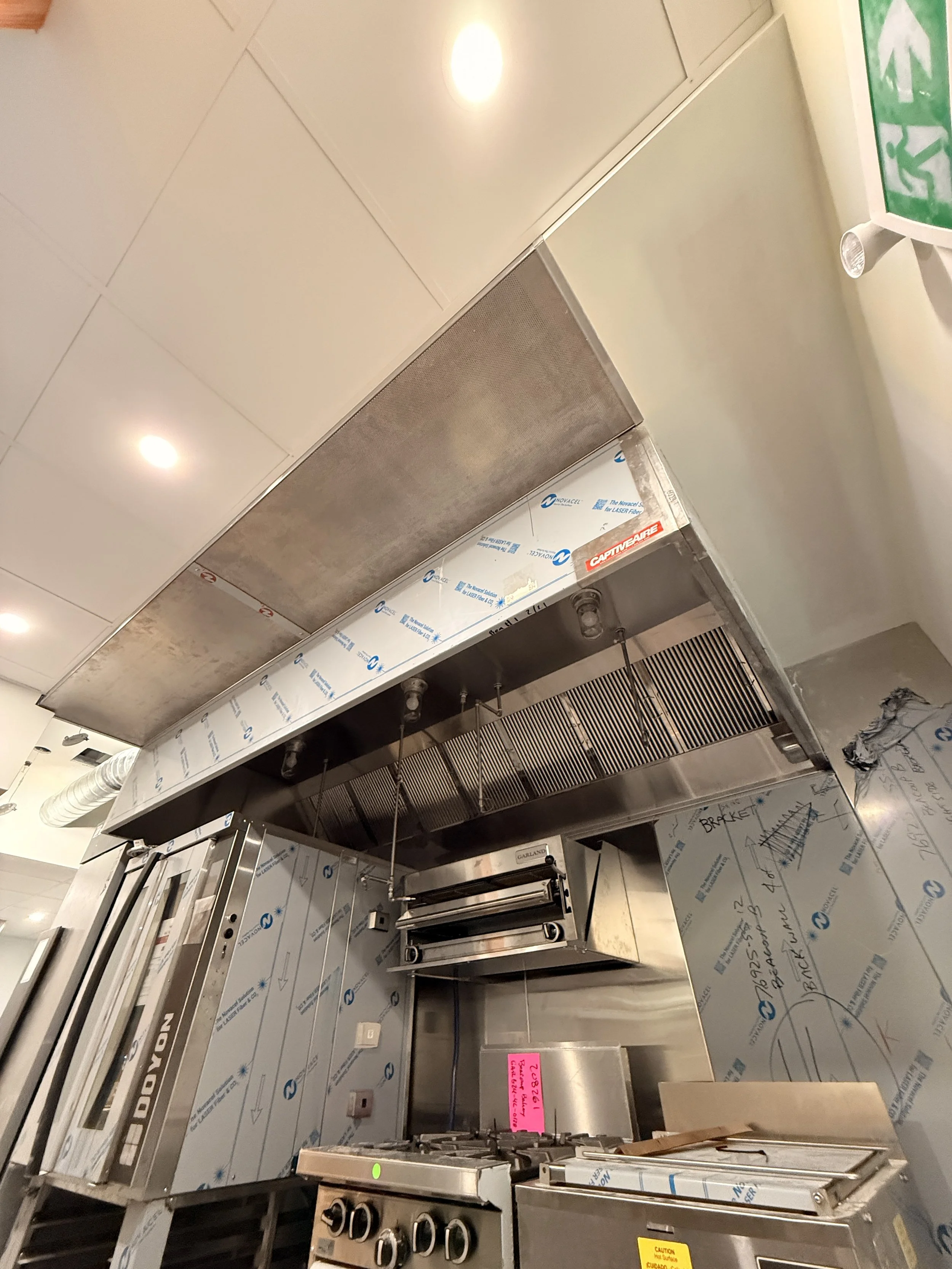 Kitchen ventilation hood and oven units under construction or installation in a commercial kitchen.