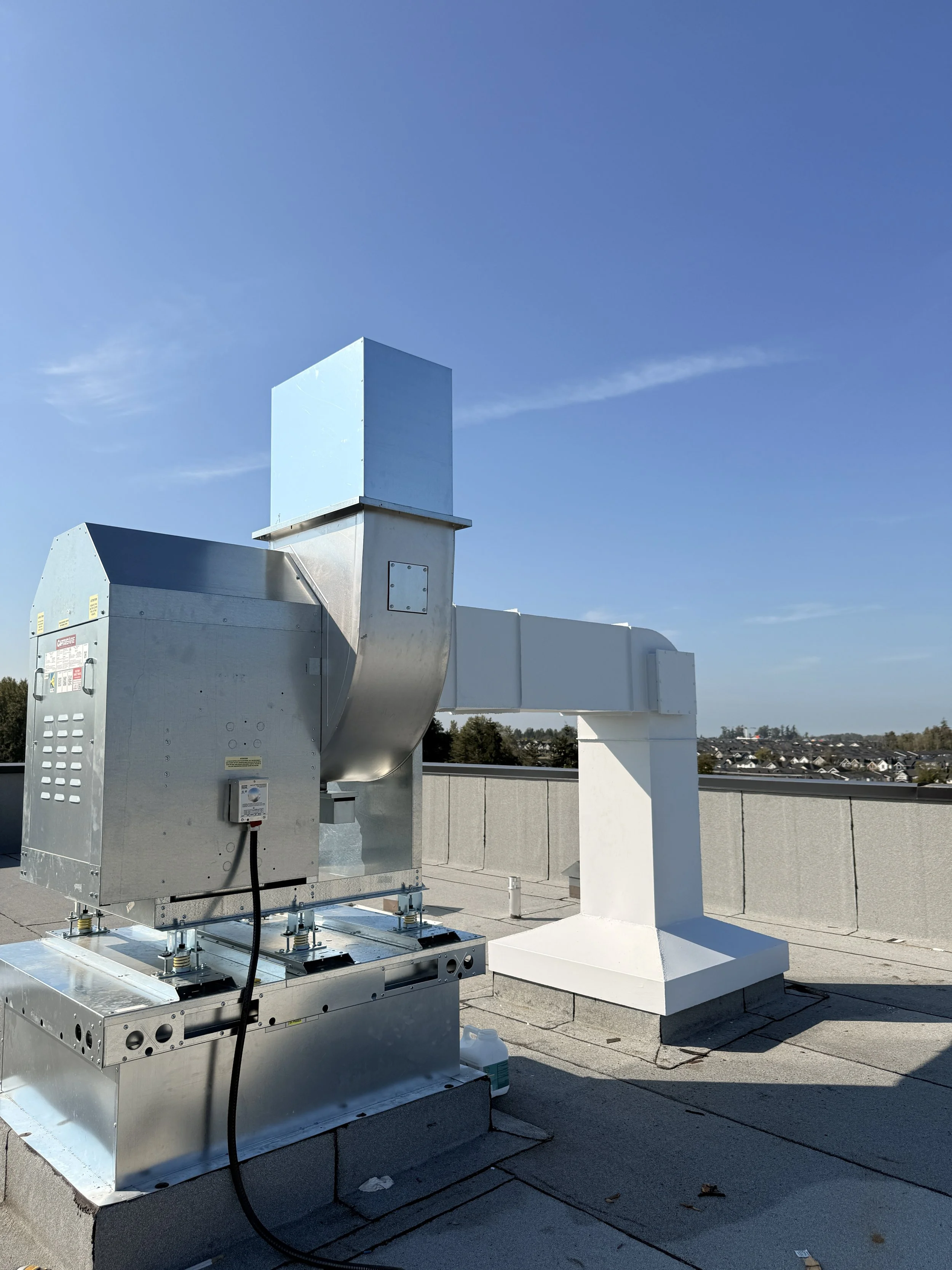 Rooftop HVAC exhaust vent system with metal ducts and vents against a blue sky.