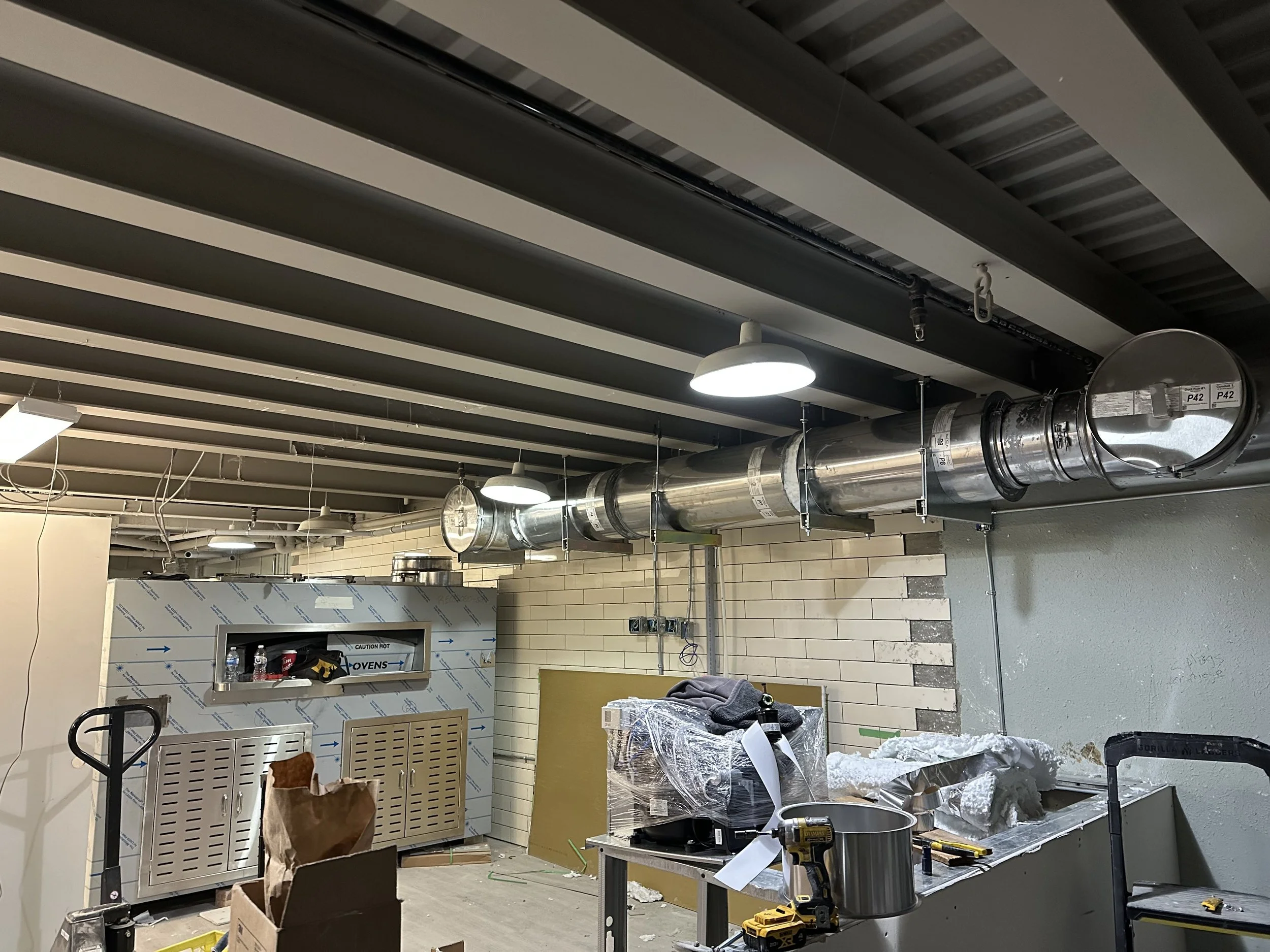 Construction site with exposed silver ventilation ductwork, drywall, tools, and a partially assembled kitchen area.