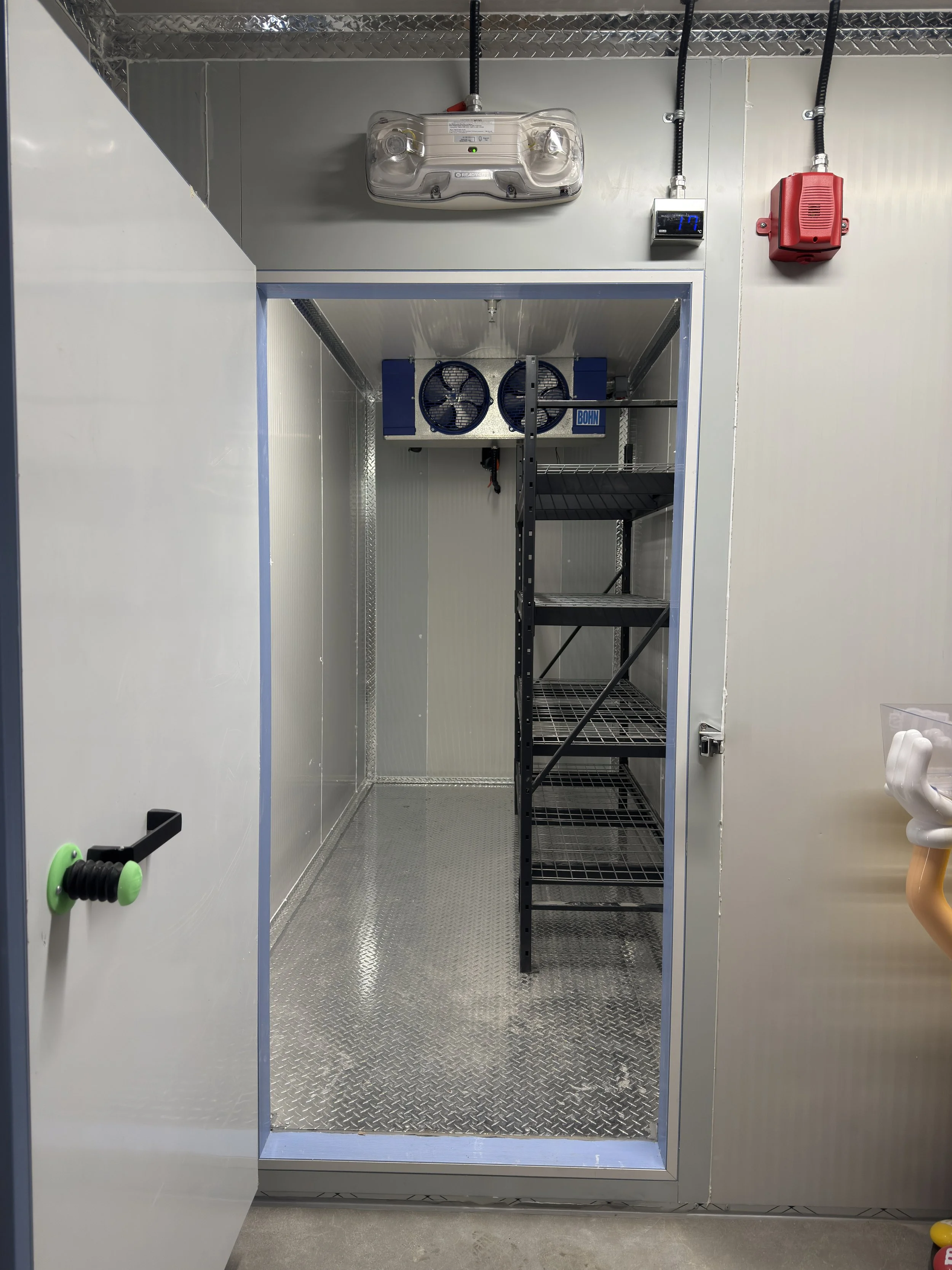 Empty walk-in freezer with metal shelves and cooling fans, located in a commercial kitchen or storage room.