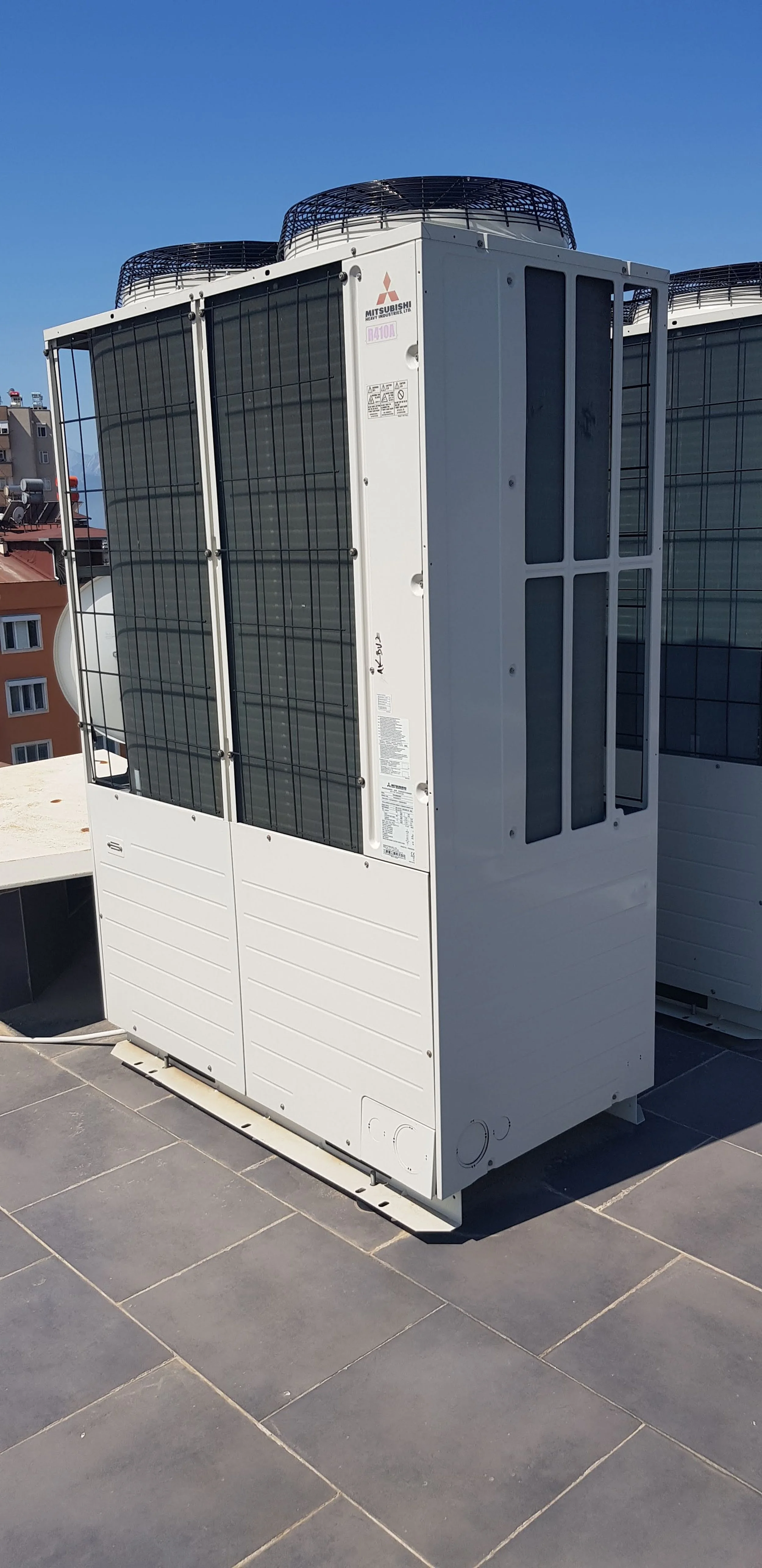 Outdoor air conditioning unit on a rooftop with a building and blue sky in the background.