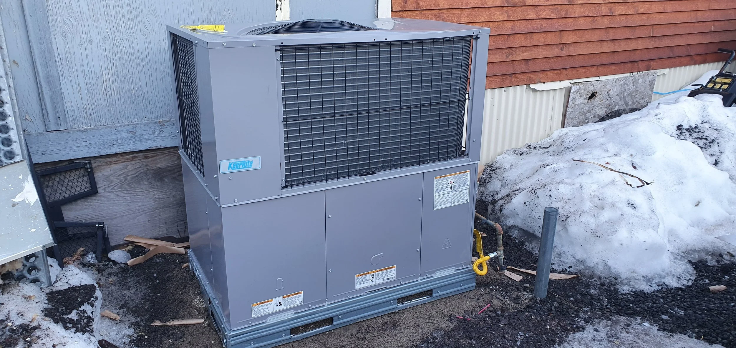 Outdoor air conditioning unit next to a building with snow on the ground.