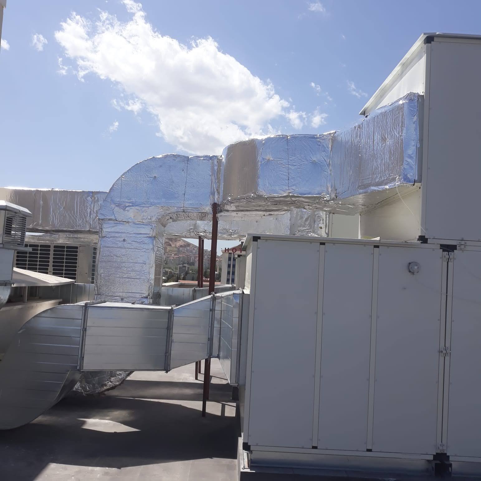 Commercial building rooftop with metal and insulated ductwork against a partly cloudy sky.