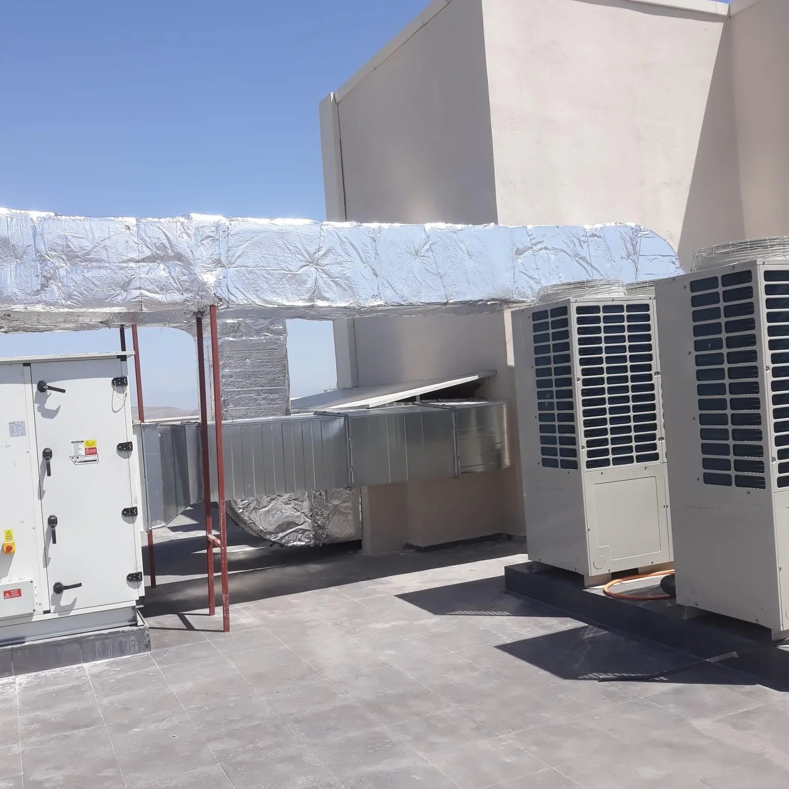 HVAC rooftop units, ductwork, and insulation on a rooftop under a clear blue sky.