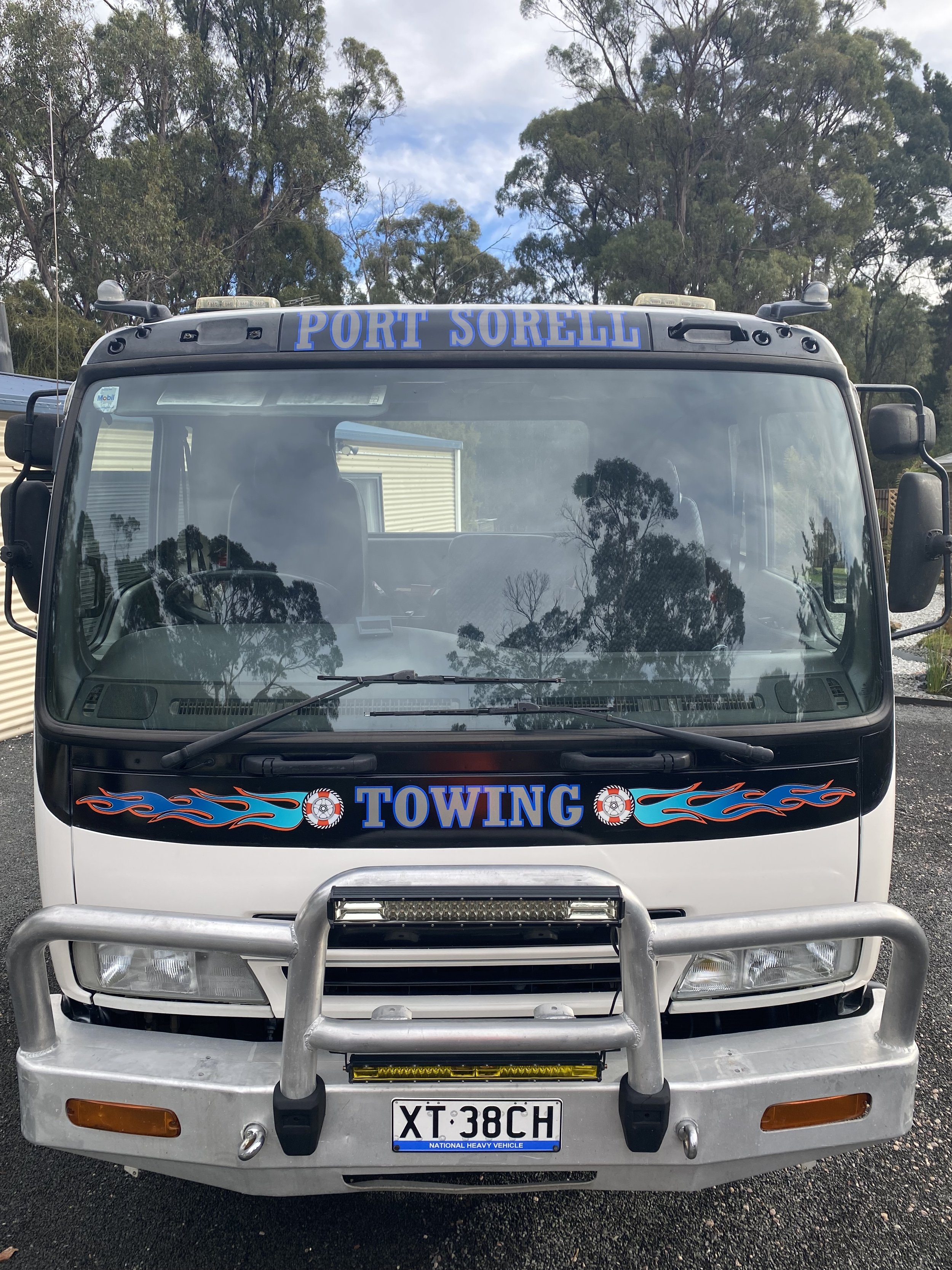 Front view of a tow truck with a black and white color scheme, blue and red flame decals, the words 'PORT SORELL' on the top, 'TOWING' in the center, and an Australian license plate 'XT 38CH'.