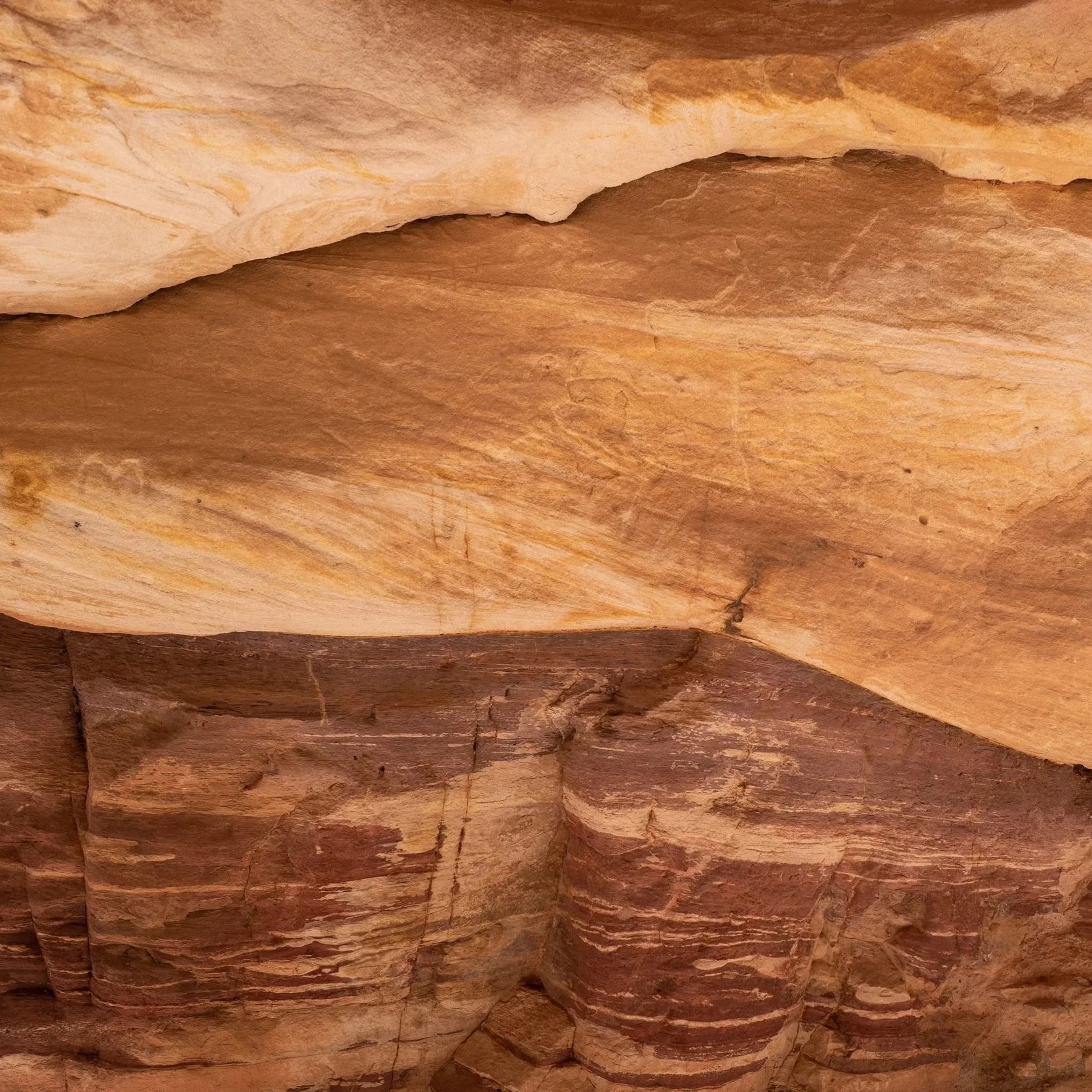 Close-up view of a layered sandstone rock formation in Jordan with varying shades of beige, reddish-brown, and purple.