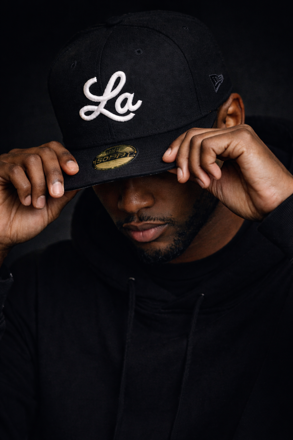 A man wearing a black LA monogram New Era 9 Fifty hat and black hoodie