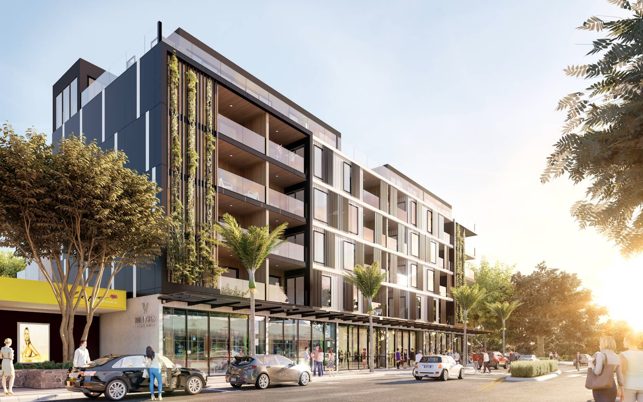 Modern multi-story building with retail shops on the ground floor, outdoor seating, and parked cars in front. Pedestrians walking along sidewalk with trees and sunlight.