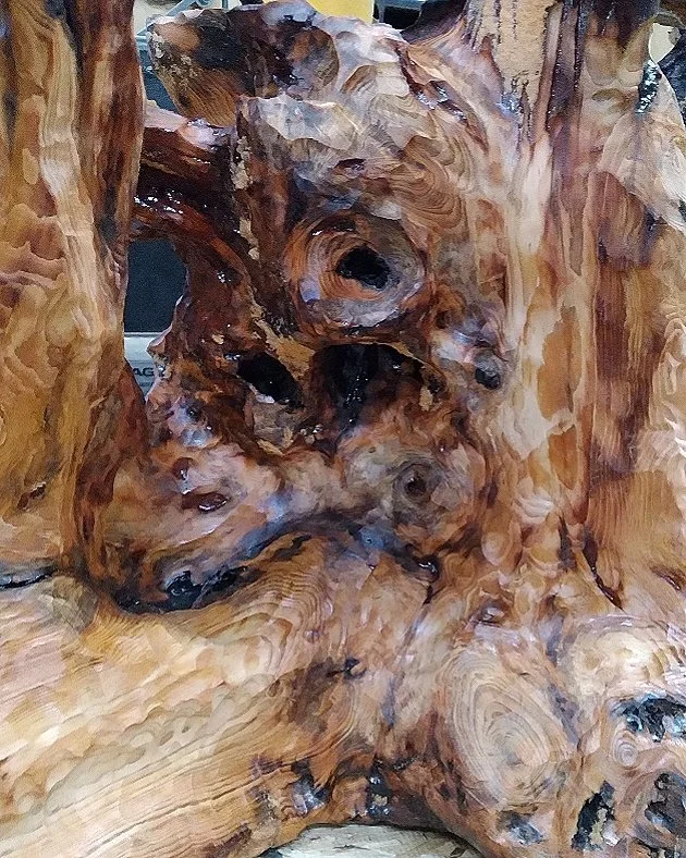 Close-up of a heavily textured, polished piece of wood with intricate knots and grain patterns.