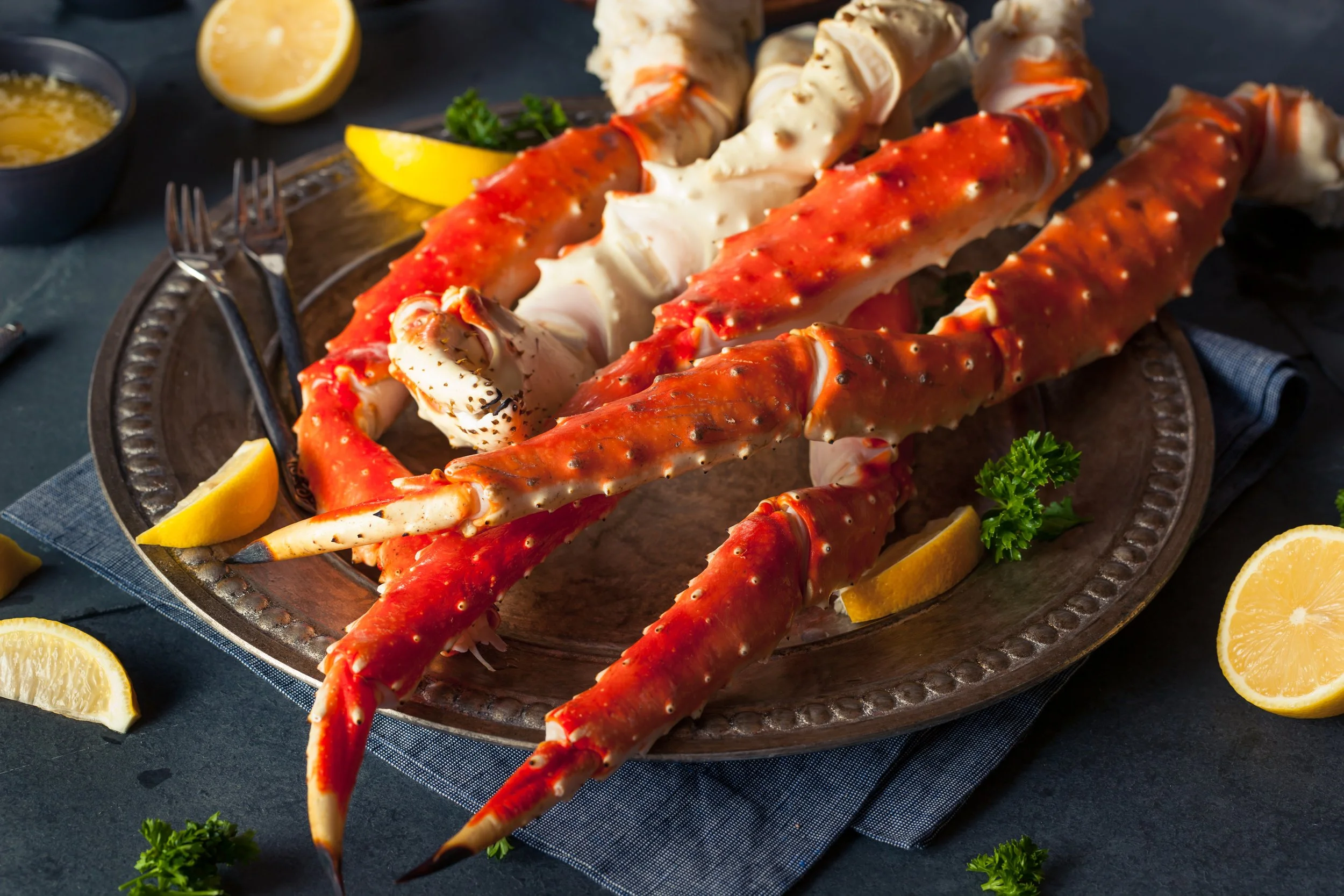 Lobster on a decorative platter with lemon wedges, parsley, and dipping sauces around it.
