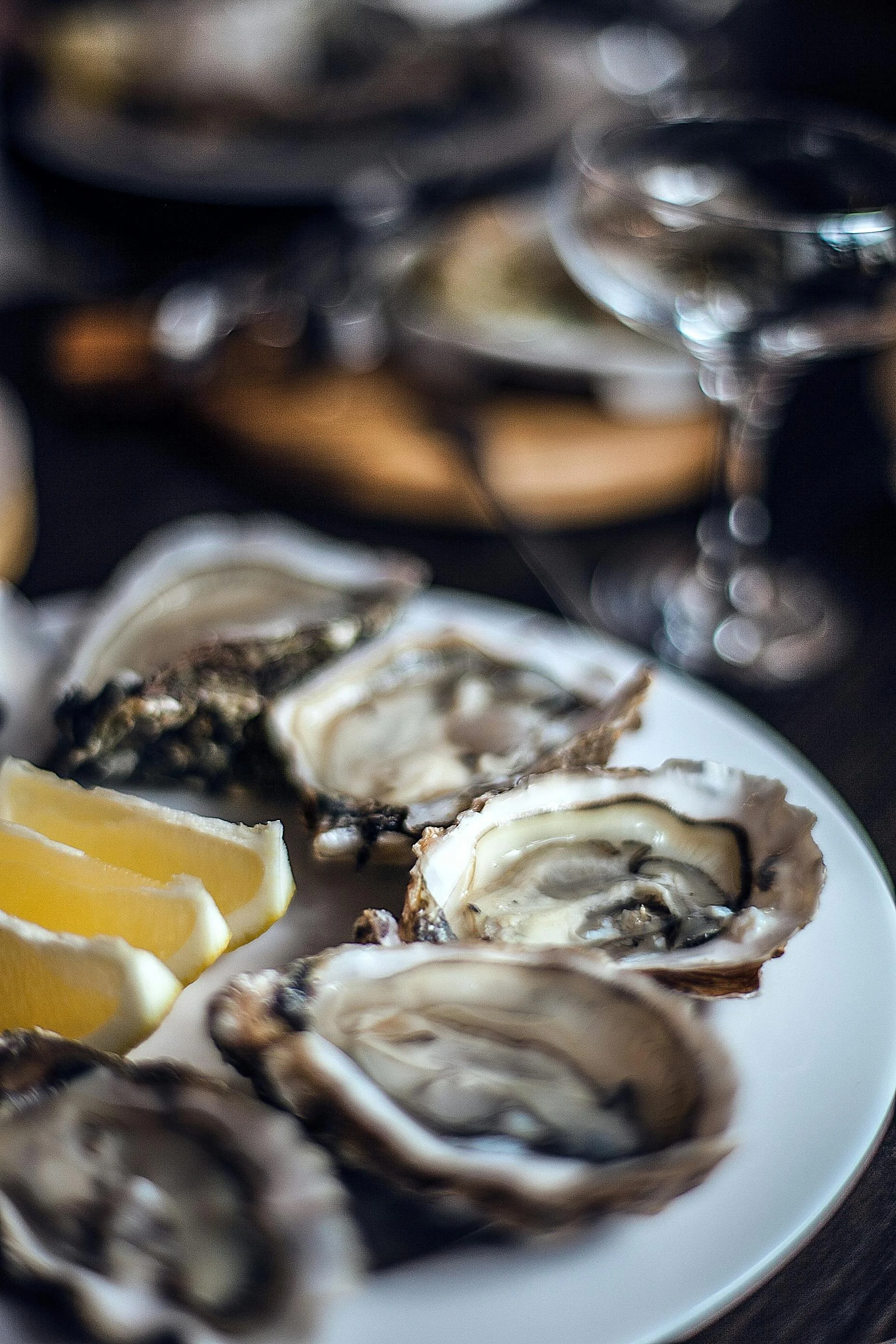 Plate of fresh oysters with lemon wedges, blurred background with wine glasses and a dark table