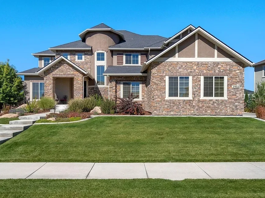 Large modern house with stone and stucco exterior, multiple gabled roof sections, and a well-maintained lawn and landscaping.