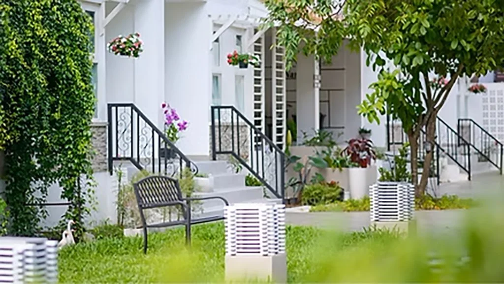 Front porch with stairs, plants, and outdoor seating in a lush garden.