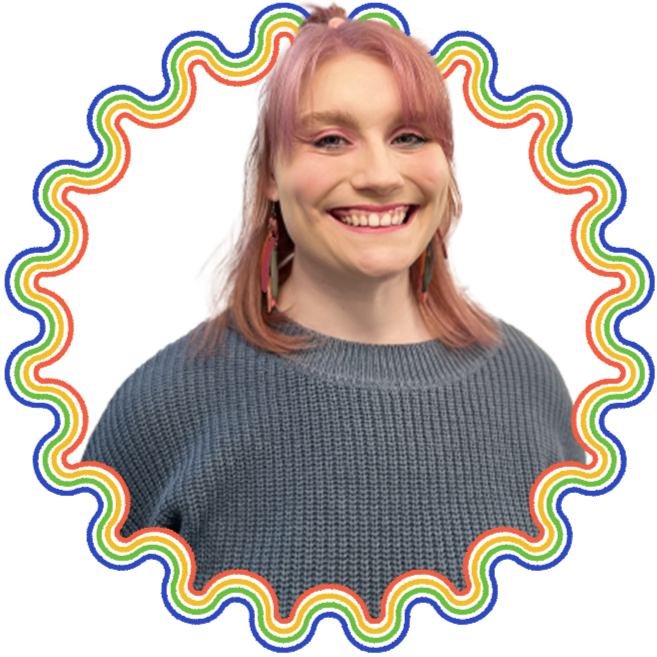 A woman with pink hair smiling, wearing a gray sweater, with colorful rainbow-colored border around her.