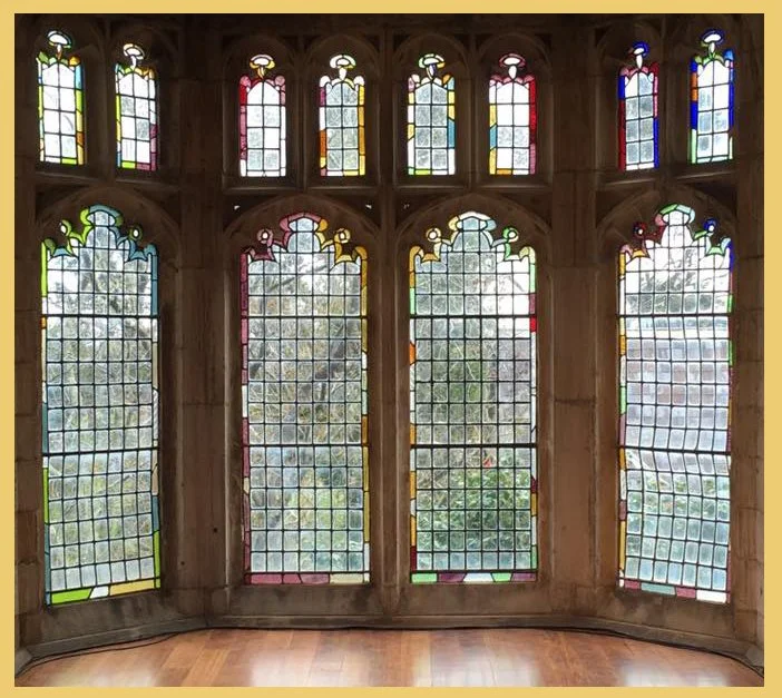 Interior view of colorful stained glass windows in a historic building, with trees visible outside.